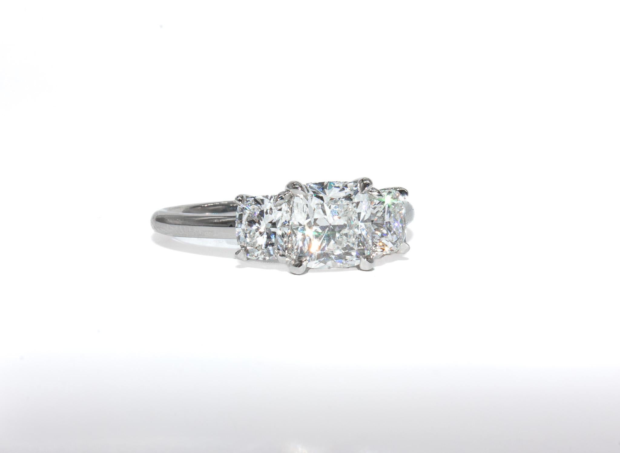 Questo squisito anello a tre pietre in platino di J. Birnbach è un design senza tempo che mette in risalto un'eccezionale maestria e brillantezza. Al centro c'è un diamante brillante a cuscino da 1,00 carati, certificato da GIA con colore G e