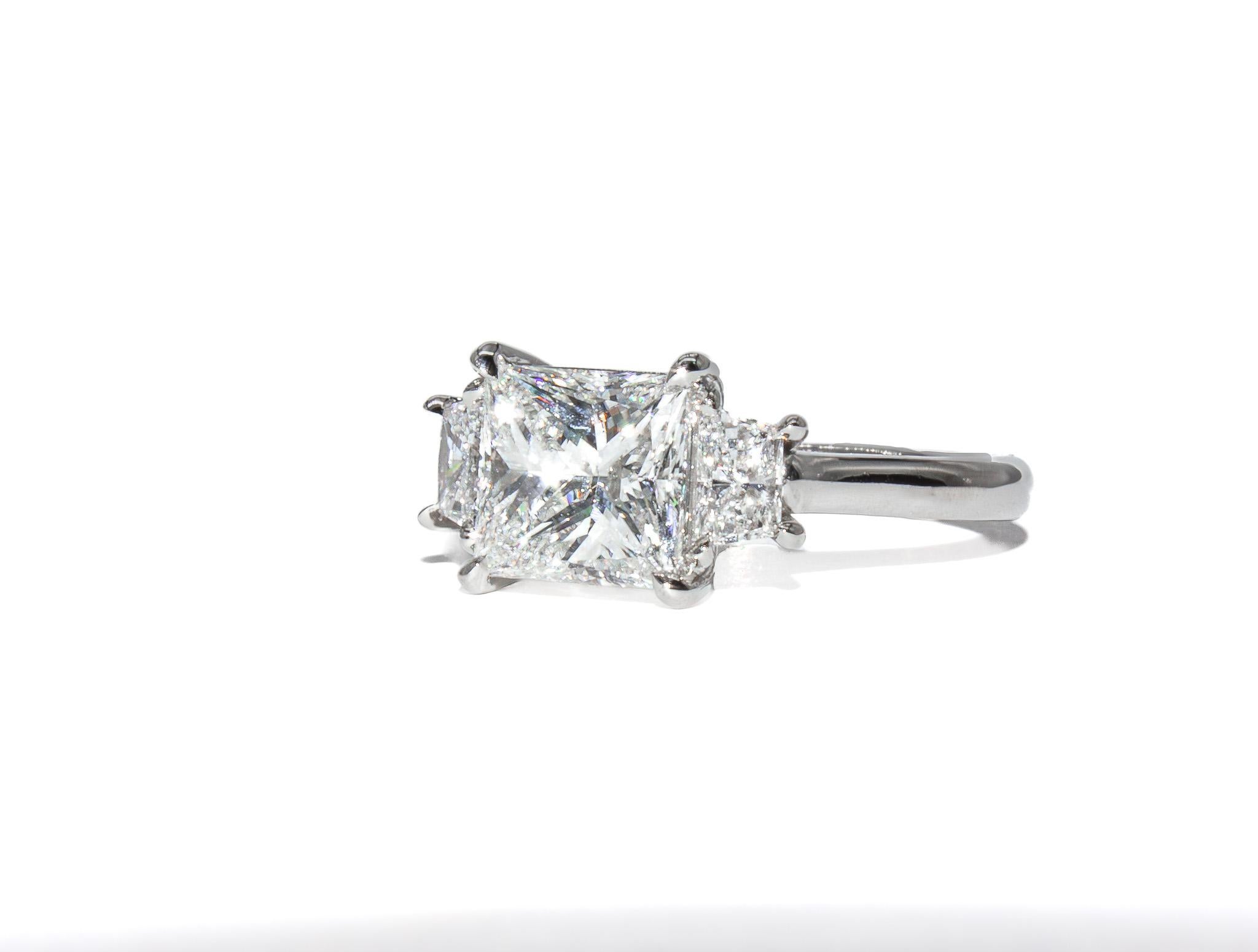 This stunning platinum three-stone ring by J. Birnbach is a timeless expression of elegance and brilliance. At the center is a dazzling 1.86 carat princess-cut diamond, certified by GIA as F color and I1 clarity. The princess cut’s sharp, angular