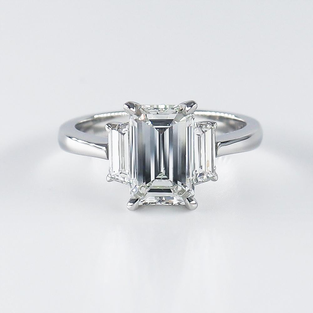 This piece is the very essence of modern elegance! This beautiful execution of the classic three-stone ring features a GIA certified 2.02 carat emerald cut diamond of G color and VS2 clarity. The diamond is uniquely narrow and elongated, giving a