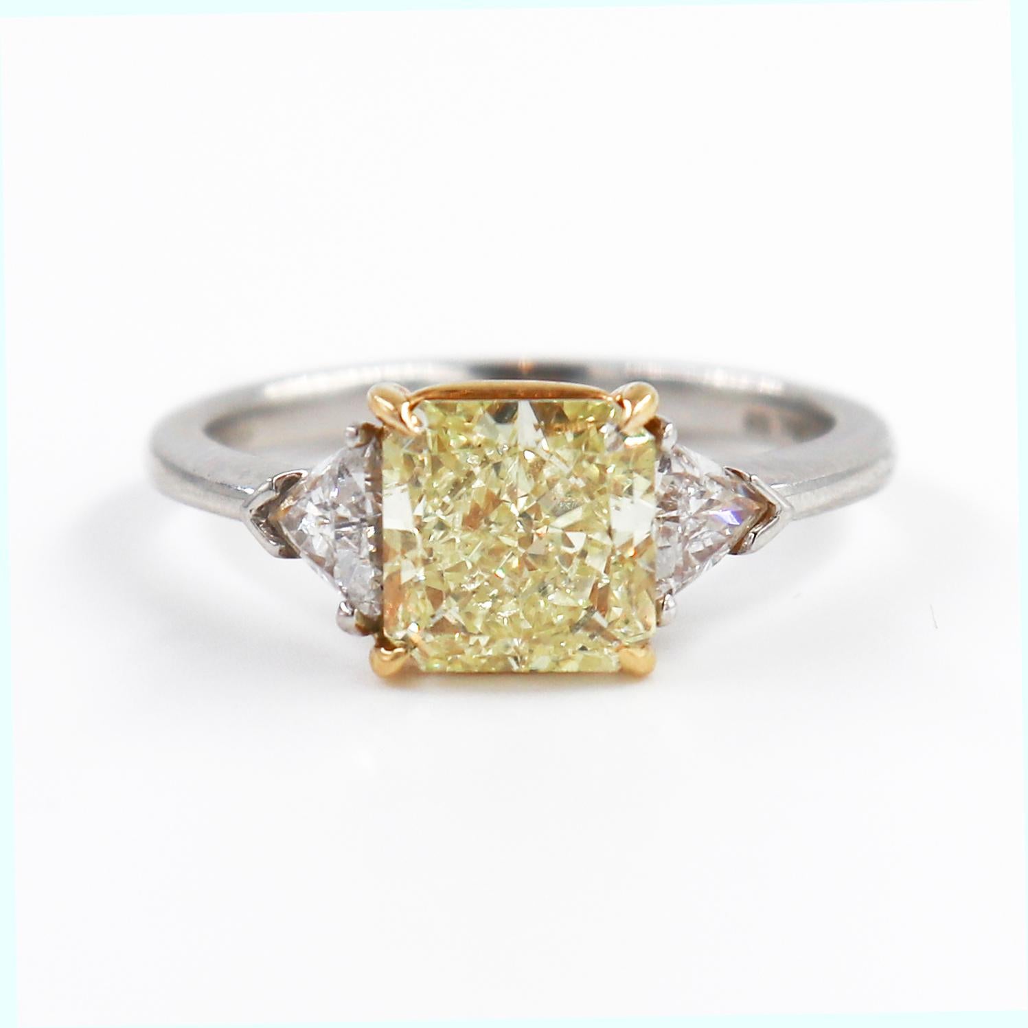 This charming ring is a fresh, bright take on the classic three stone design. It features a 2.03 carat radiant diamond certified by GIA to be a fancy yellow color. This brilliant, saturated radiant diamond contrasts beautifully with the bright white