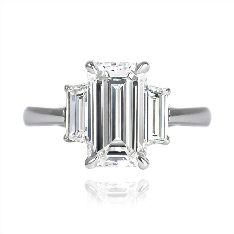 This scintillating, step-cut stone is a GIA certified 2.04 carat Emerald cut diamond of E color and SI1 clarity... Set in a handmade, platinum three-stone ring with trapezoid side stones = 0.80 ctw, this ring's geometry is simply mesmerizing from