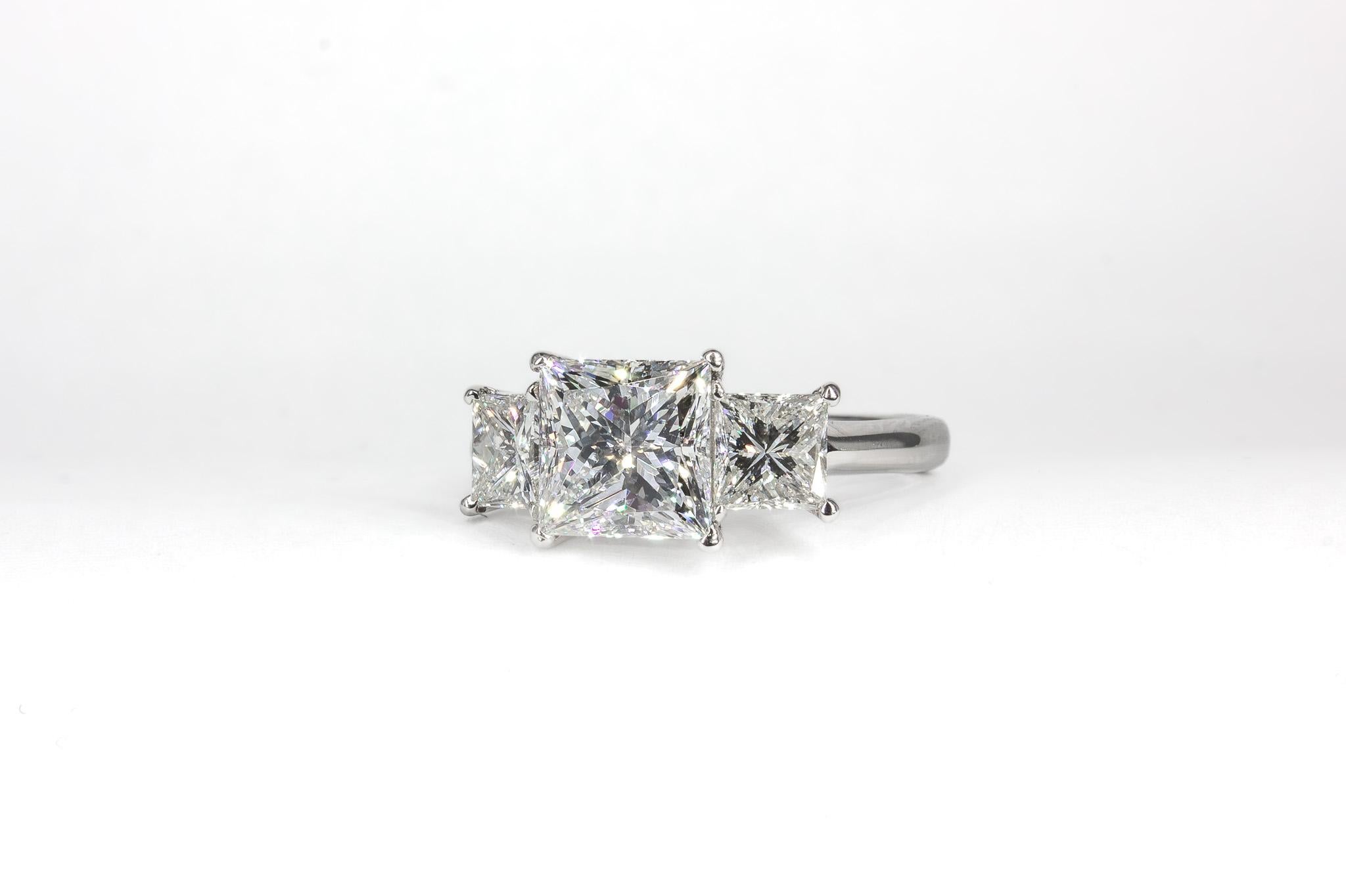 This elegant platinum three-stone ring showcases a dazzling 2.09-carat princess-cut diamond, certified by GIA as F color with SI1 clarity. The crisp, geometric facets of the center stone create exceptional brilliance, enhanced by two perfectly