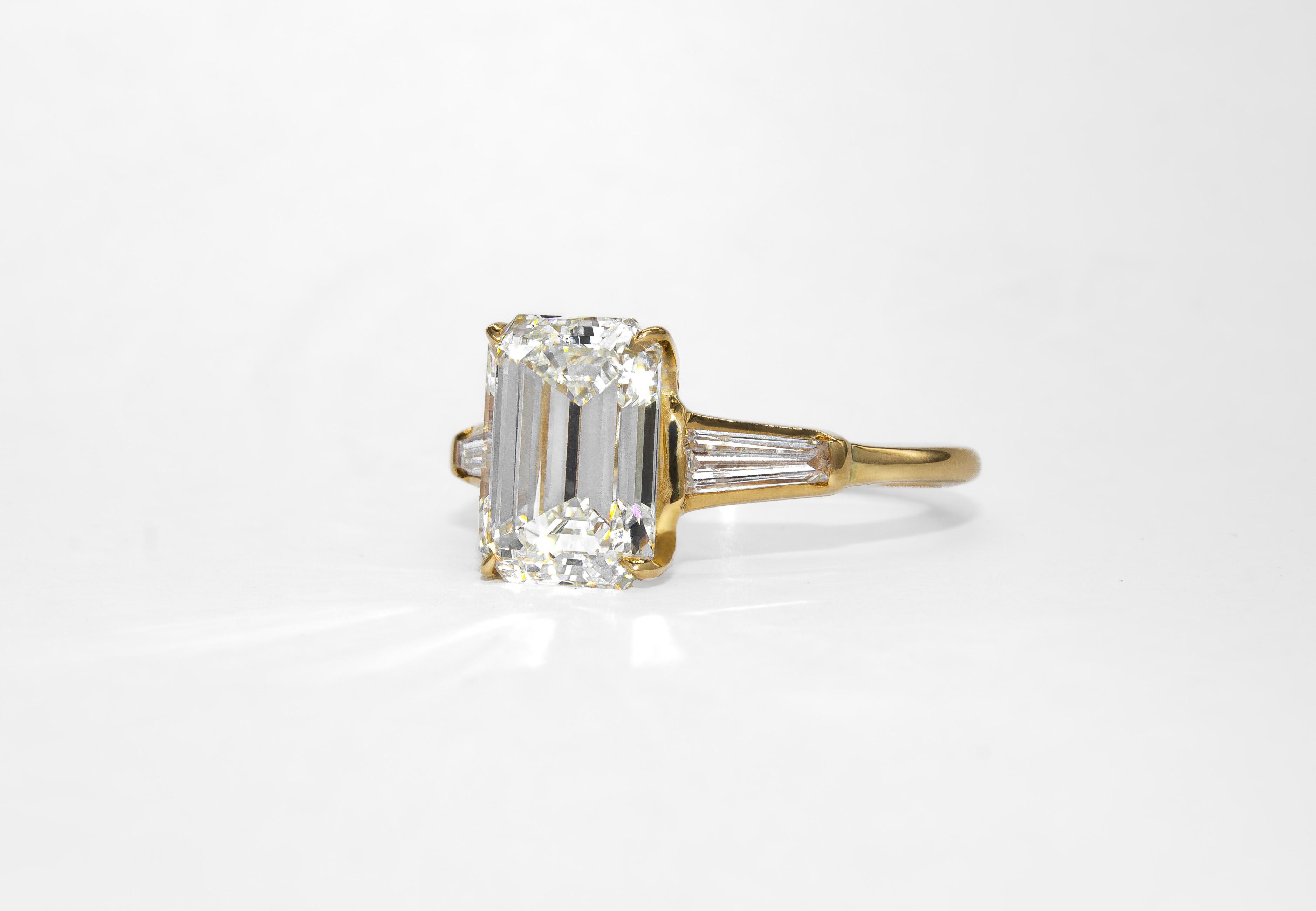 This timeless three-stone engagement ring is crafted in a soft 14K yellow gold alloy, thoughtfully chosen to enhance the warm tone of the center diamond. At the heart is a 2.66 carat emerald cut diamond, graded by GIA as J color and VS2 clarity. Its
