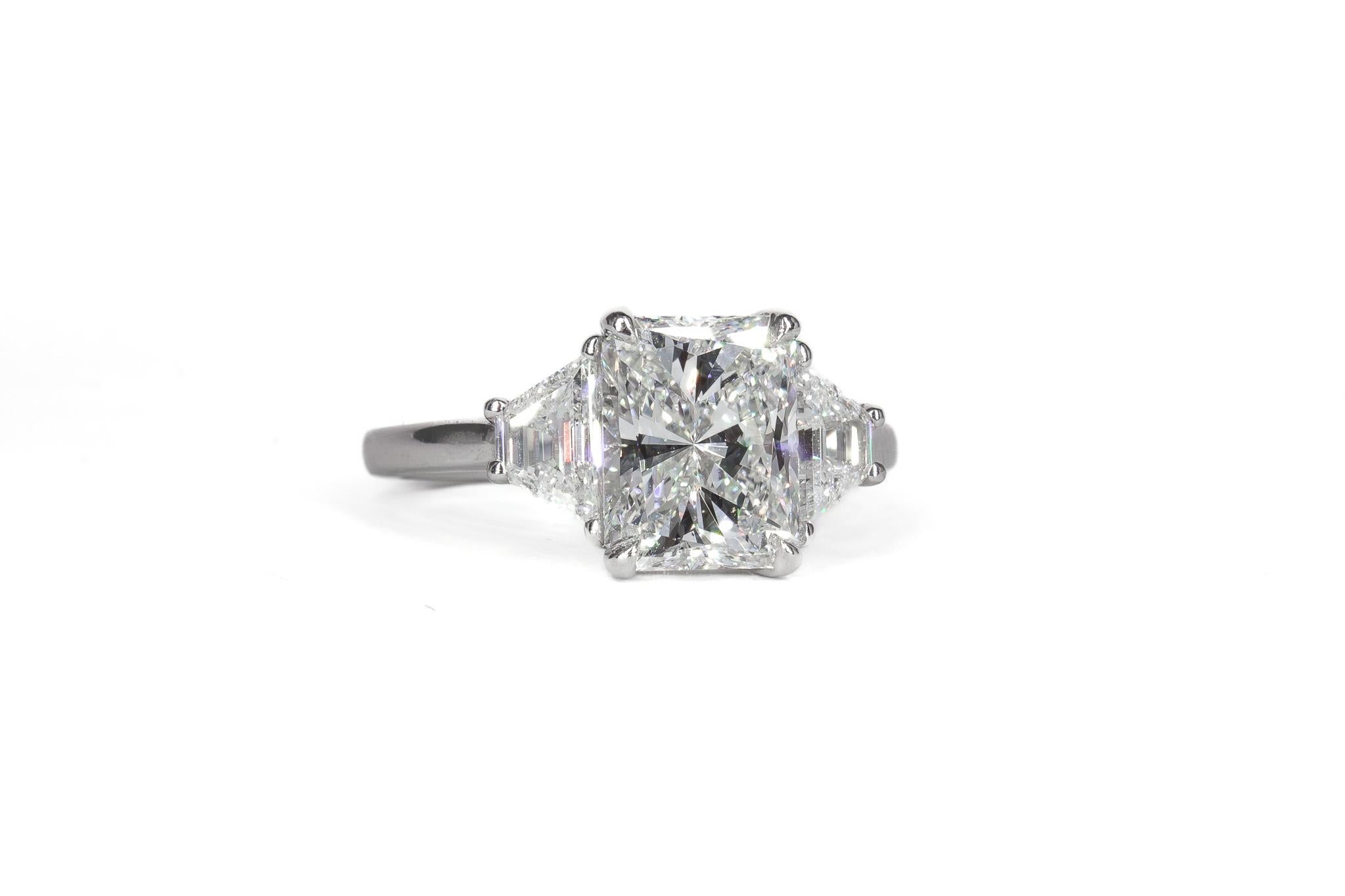 Cette exquise bague en platine à trois pierres met en valeur un superbe diamant radiant de 2,30 carats, certifié par le GIA de couleur F et de pureté VVS2. Les facettes nettes et la brillance exceptionnelle du diamant central sont magnifiquement