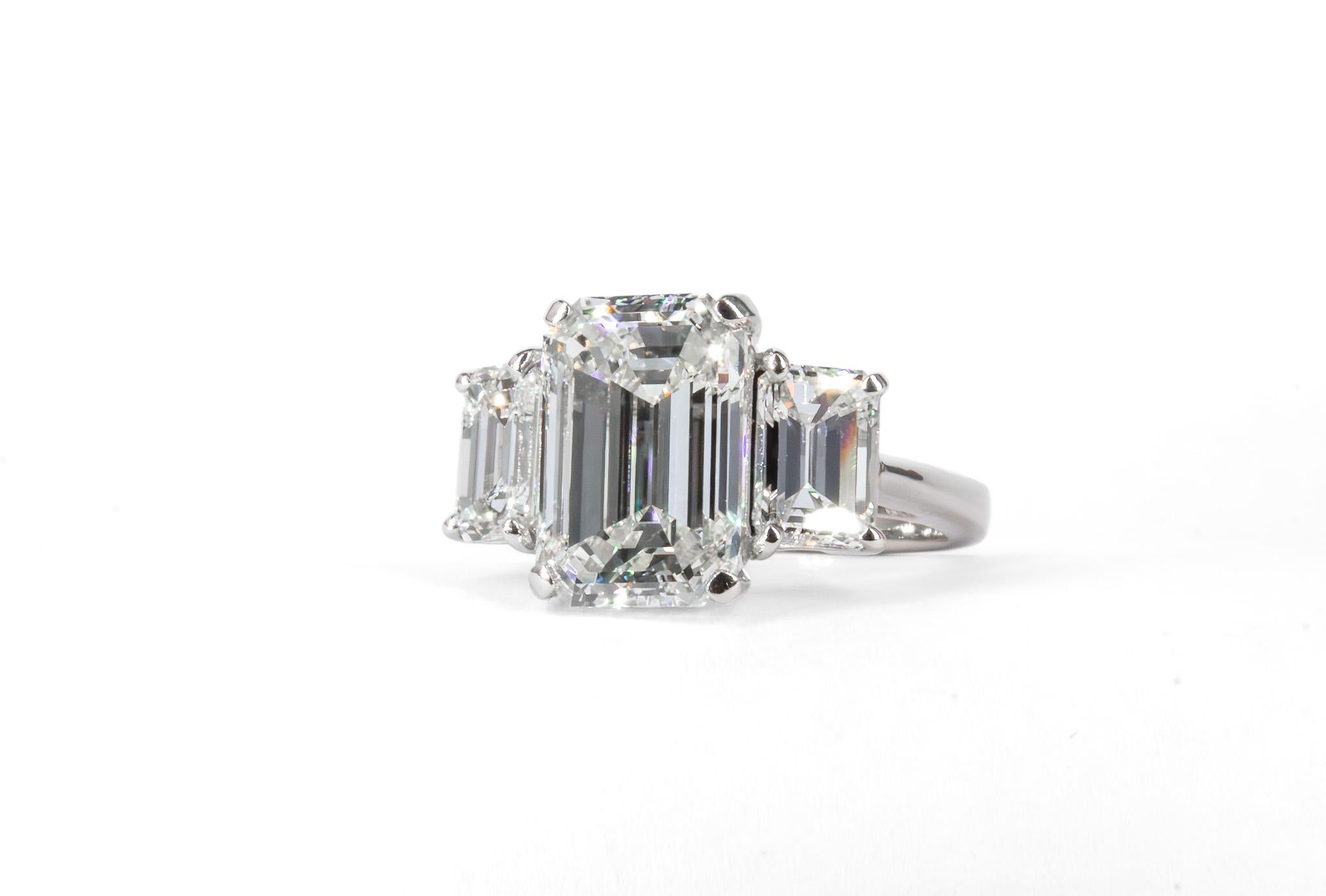 This exquisite platinum three-stone ring showcases a remarkable 4.53 carat emerald cut diamond with K color and VS2 clarity, certified by GIA. The center stone is beautifully complemented by two matching emerald cut side diamonds, weighing 0.96 and