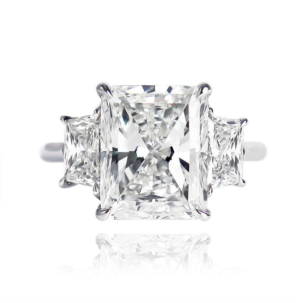 This scintillating beauty features a GIA certified 5.01 carat Radiant cut diamond of I color and SI1 clarity.  Set in a platinum, handmade three-stone ring with brilliant-cut trapezoid side stones that total  1.12 carats, this stunning piece makes a