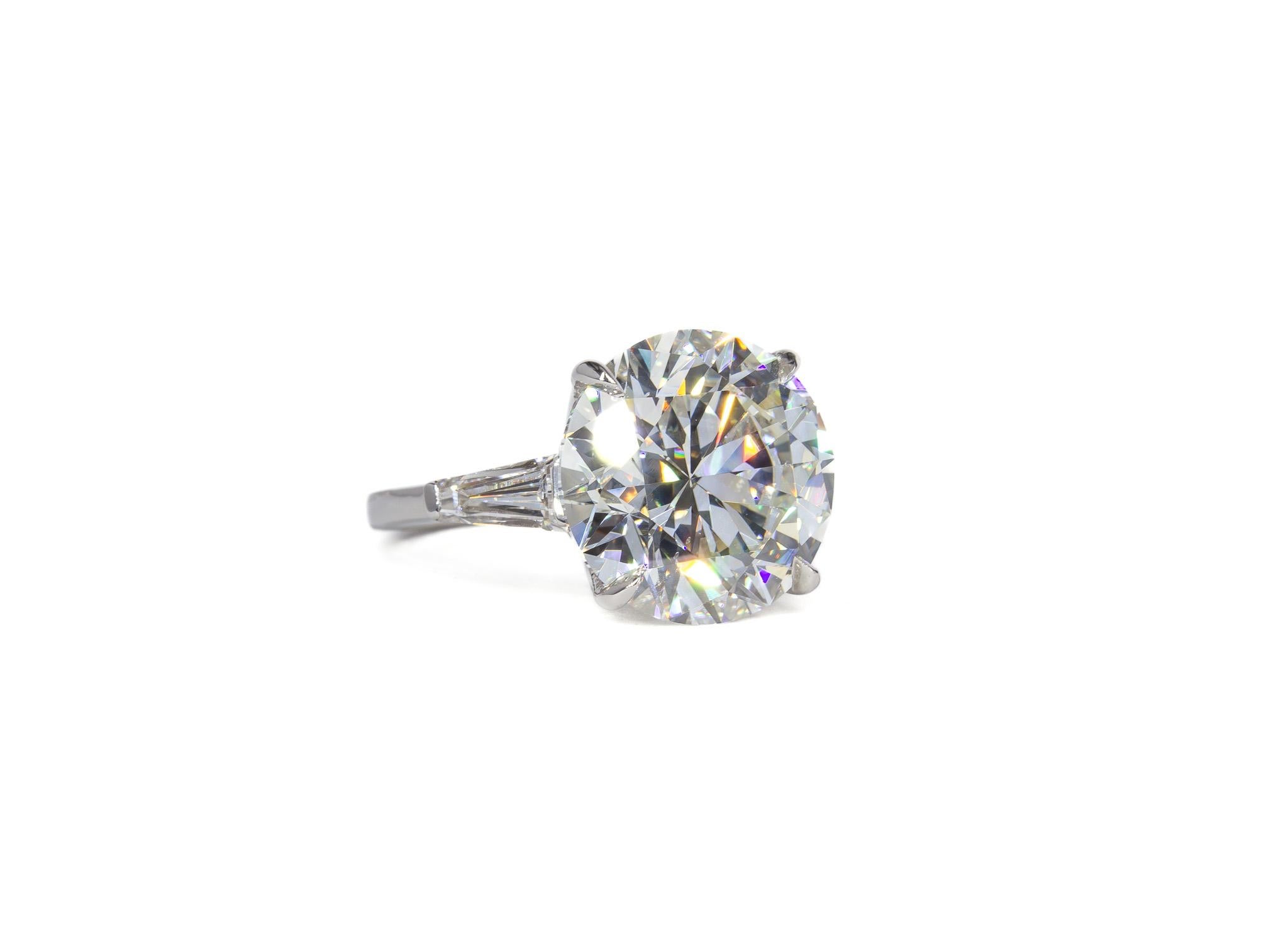 This stunning platinum three-stone ring is a true celebration of timeless elegance and brilliance. At its center is a magnificent 7.54 carat round brilliant diamond, GIA-certified with an I color and SI1 clarity, radiating exceptional fire and
