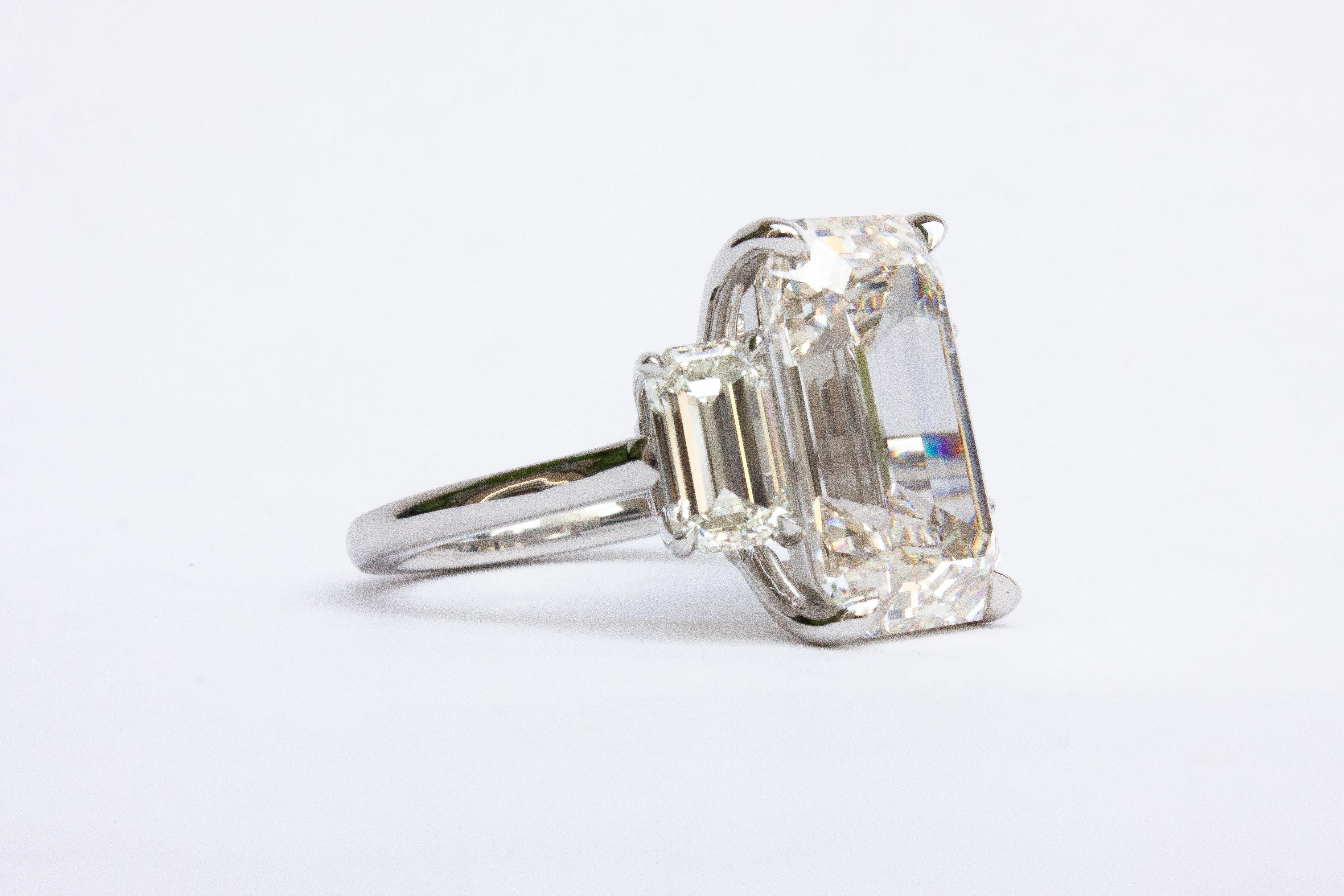 This extraordinary platinum three-stone ring is a masterpiece of timeless elegance and brilliance. At its center is a breathtaking 8.04 carat emerald cut diamond, graded J color and VS1 clarity by GIA, radiating sophisticated beauty with its crisp,