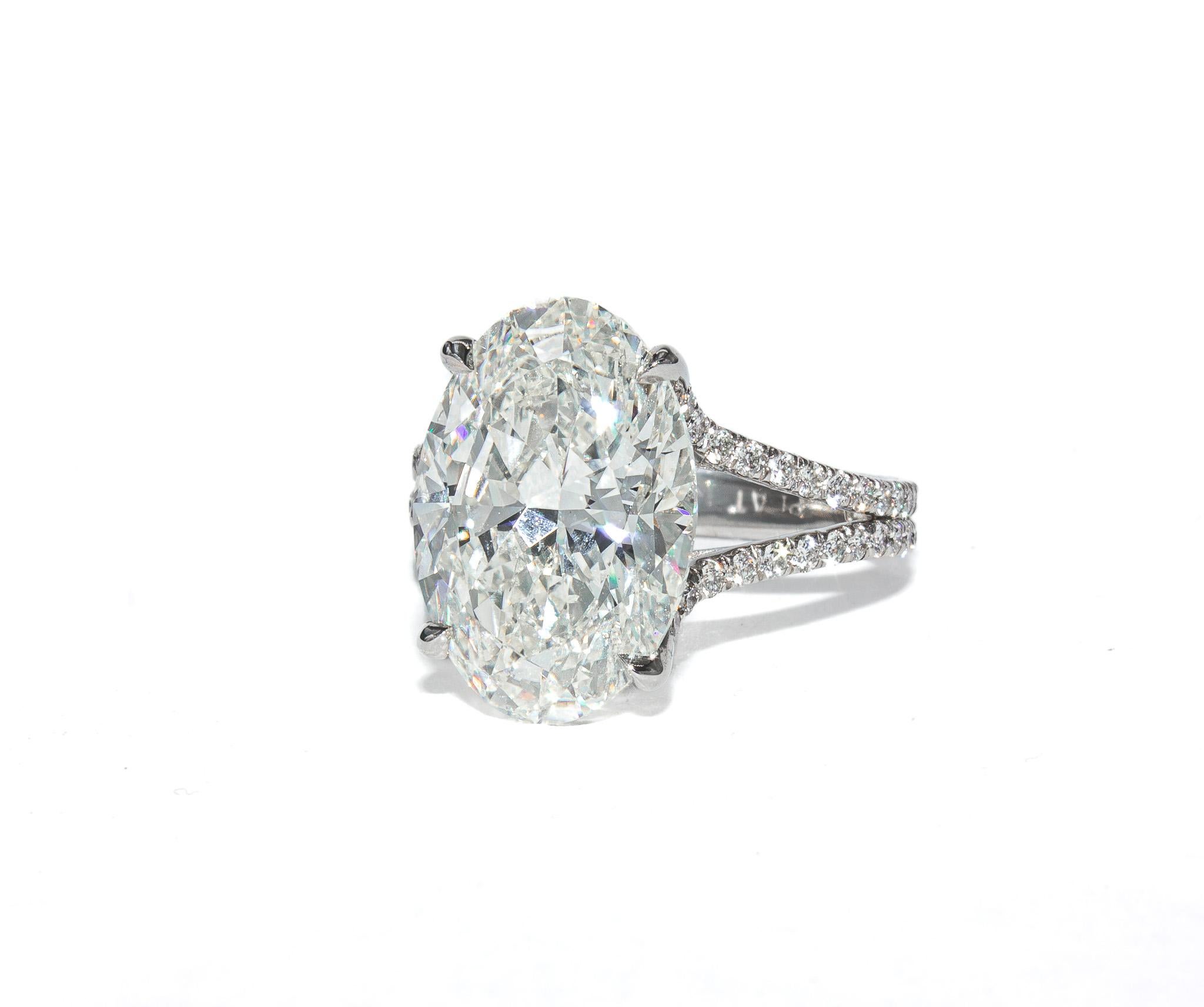 This striking platinum split shank ring centers on a remarkable 6.04 carat oval cut diamond, graded K color and SI2 clarity by GIA. The elongated oval shape offers exceptional finger coverage and a graceful, elegant silhouette. The center stone is