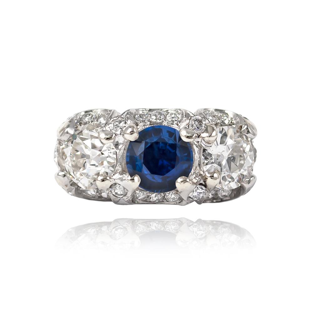 This antique from the J. Birnbach vault features a vibrant, blue sapphire = 1.84 cts & a pair of Old European cut diamond side stones = 2.20 ctw (approximately) of H-I color and SI clarity. Delightfully charming with hand-engraved & scalloped pavé