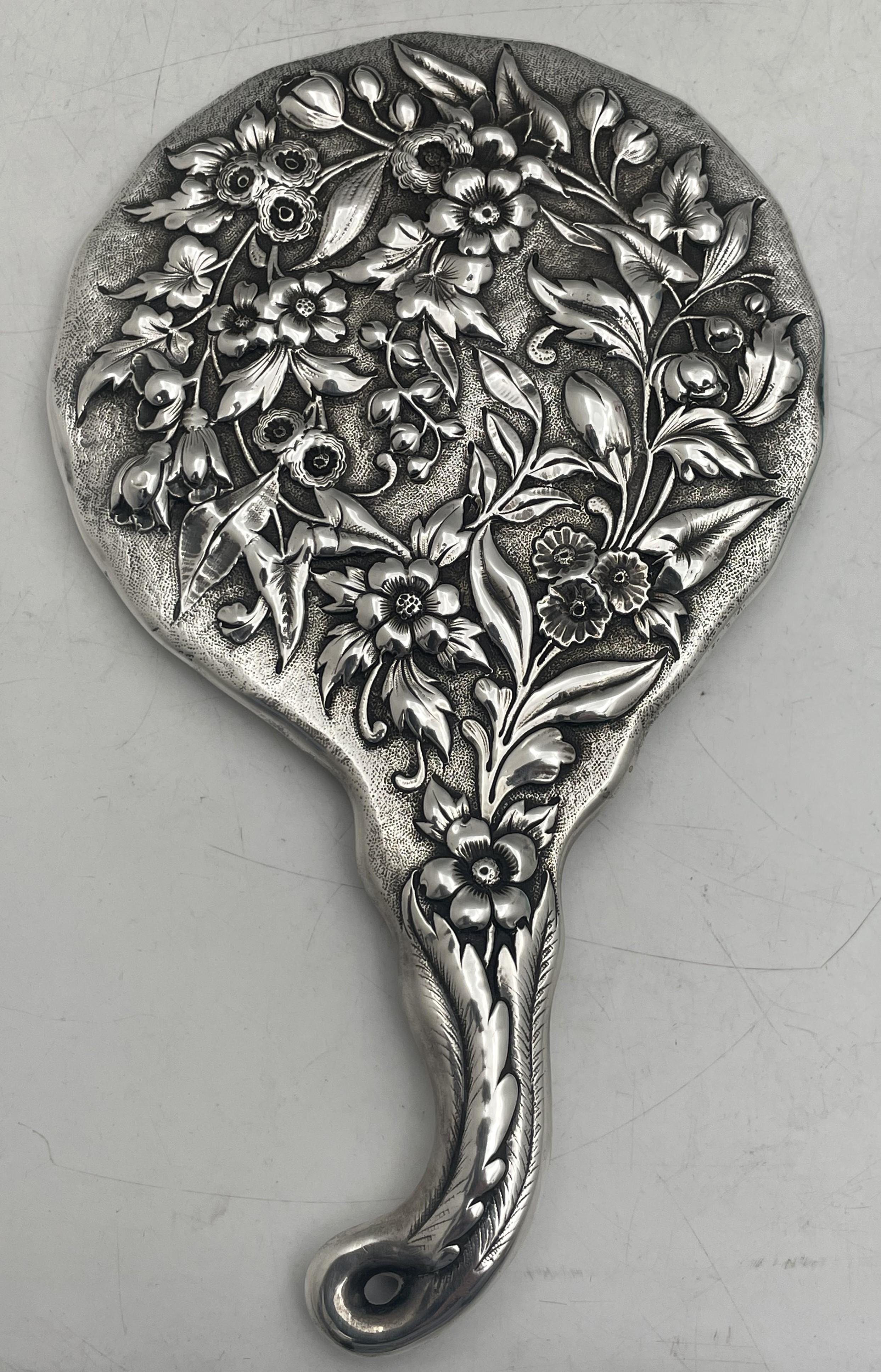 J. E. Caldwell & Co. sterling silver mirror in repousse pattern, beautifully adorned with floral motifs on the back and on the handle, from the late 19th century. It measures 9 3/8'' in length by 5 5/8'' in width by 5/8'' in depth and bears