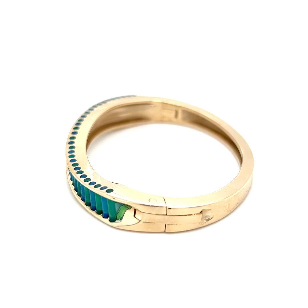 One 14 karat yellow gold wave design hinged bangle bracelet from world-renowned designer John Kennedy featuring 31 alternating blue and green onyx gemstones in Kennedy’s patented cylettes (cylindrical) cut. The bracelet measures 2.5″.

Stamped “14K