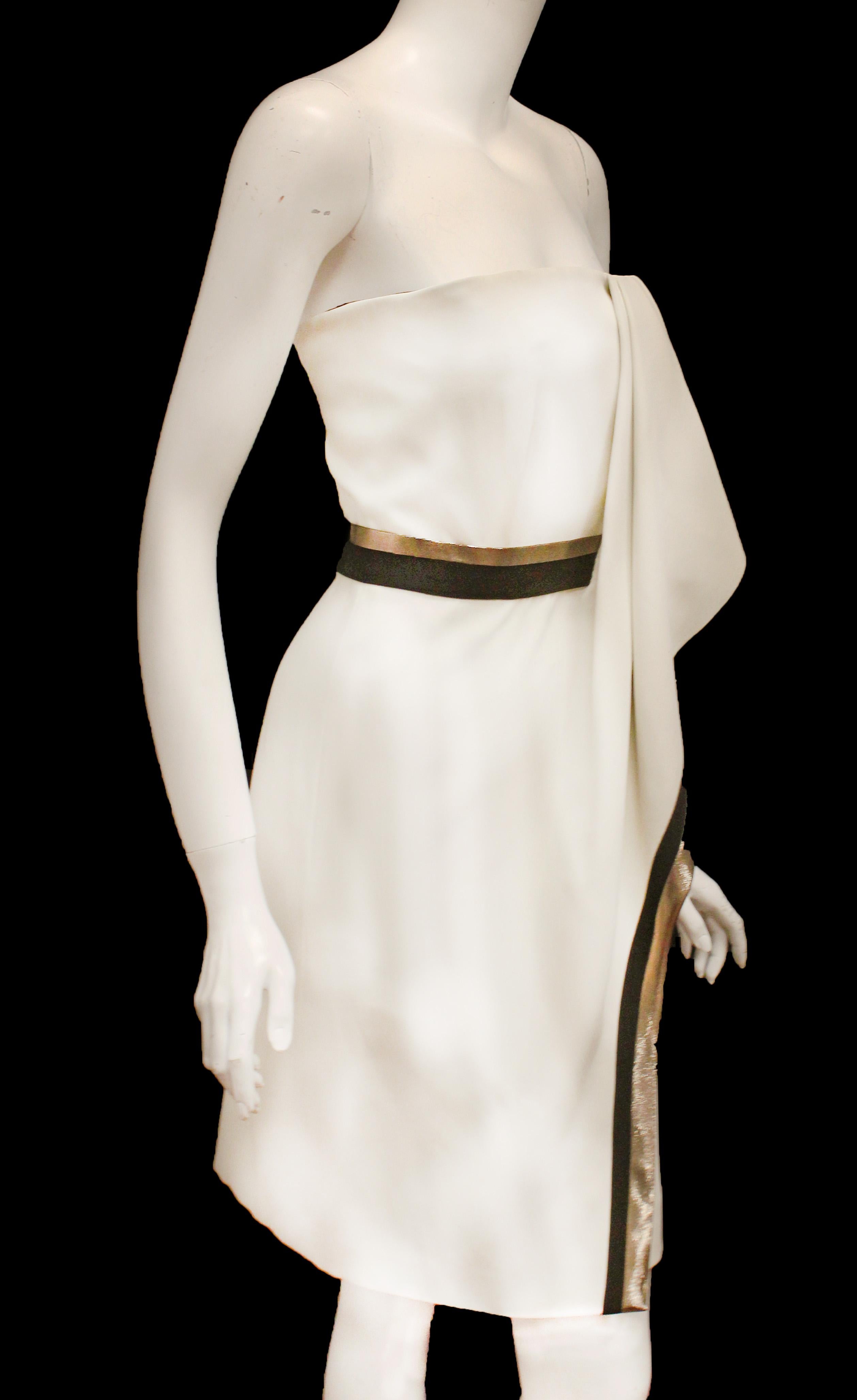 J. Mendel ivory strapless silk dress is  trimmed at waist and, also, down the draped detail at front in black and metallic gold tone strips.  The hemline is asymmetrical with the draped detail falling lower than the rest of dress.  The bodice