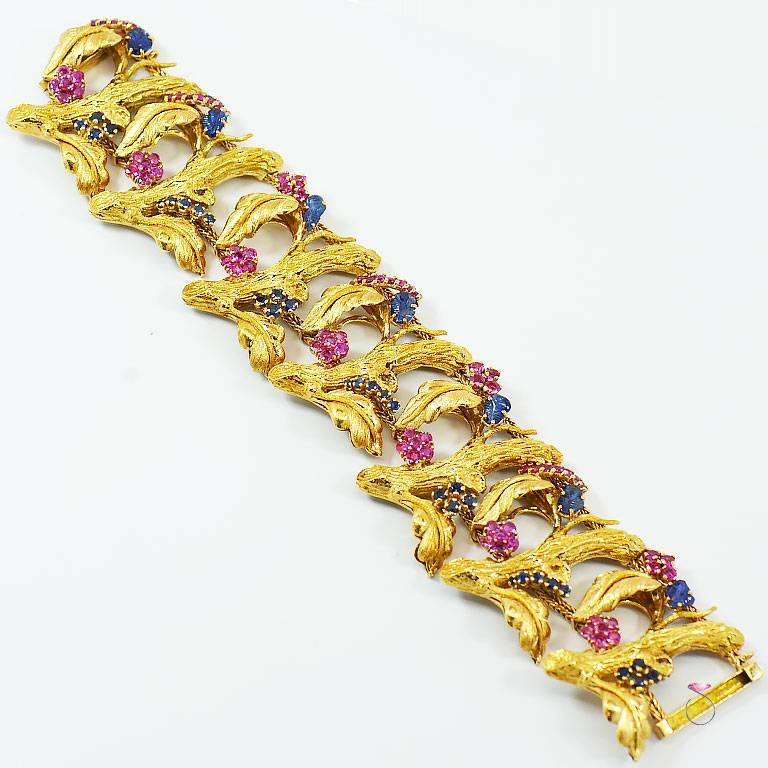 Vintage J. Rossi wide Bracelet in 18K Yellow Gold with Rubies and blue Sapphires in a beautiful floral botanical Design. This gorgeous bracelet features masterfully carved blue Sapphires in a leaf design that complements the bark and leaf designs on