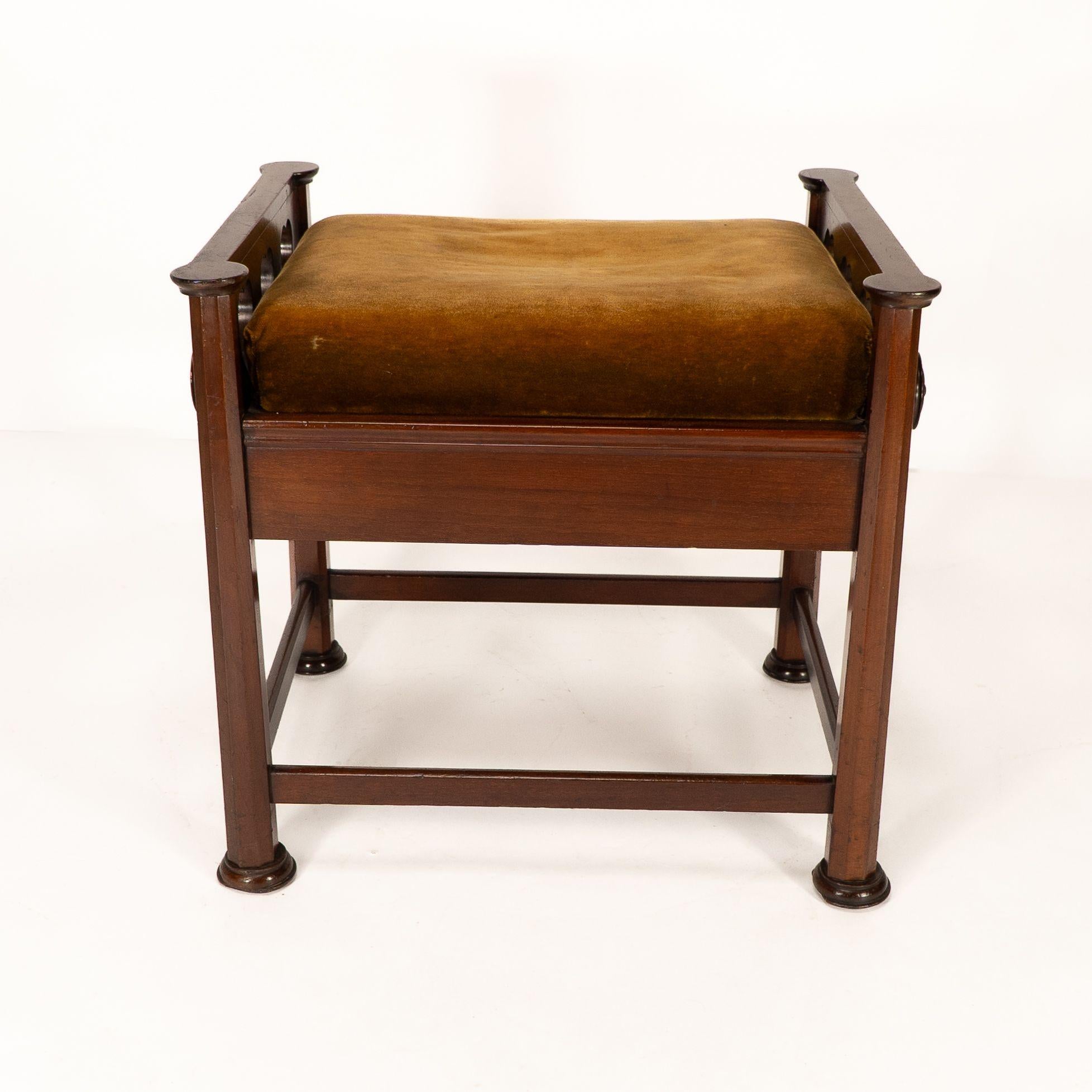 J.S. Henry al estilo de Voysey. Taburete de piano regulable Arts and Crafts, de nogal, con decoración de corazones perforados a los lados y asas redondas extendidas regulables en altura a cada lado que conectan con un ''mecanismo de asiento