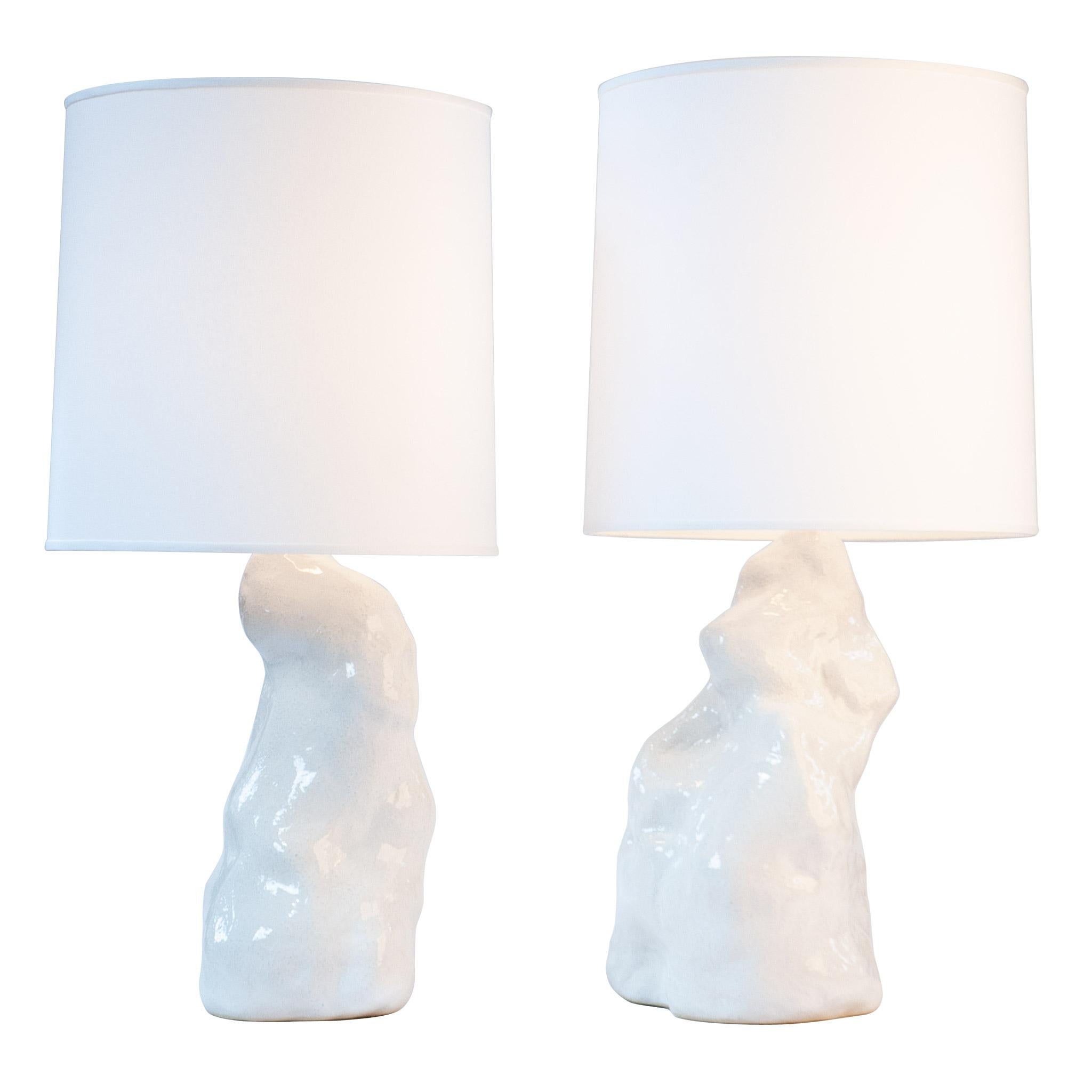 The white amorphous lamp pair ground and illuminate a room. Hand-sculpted from textured stoneware clay and fired with a lustrous milky finish. hand-sculpted stoneware lamp bases, white linen textured fabric shades, fully dimmable UL listed sockets,