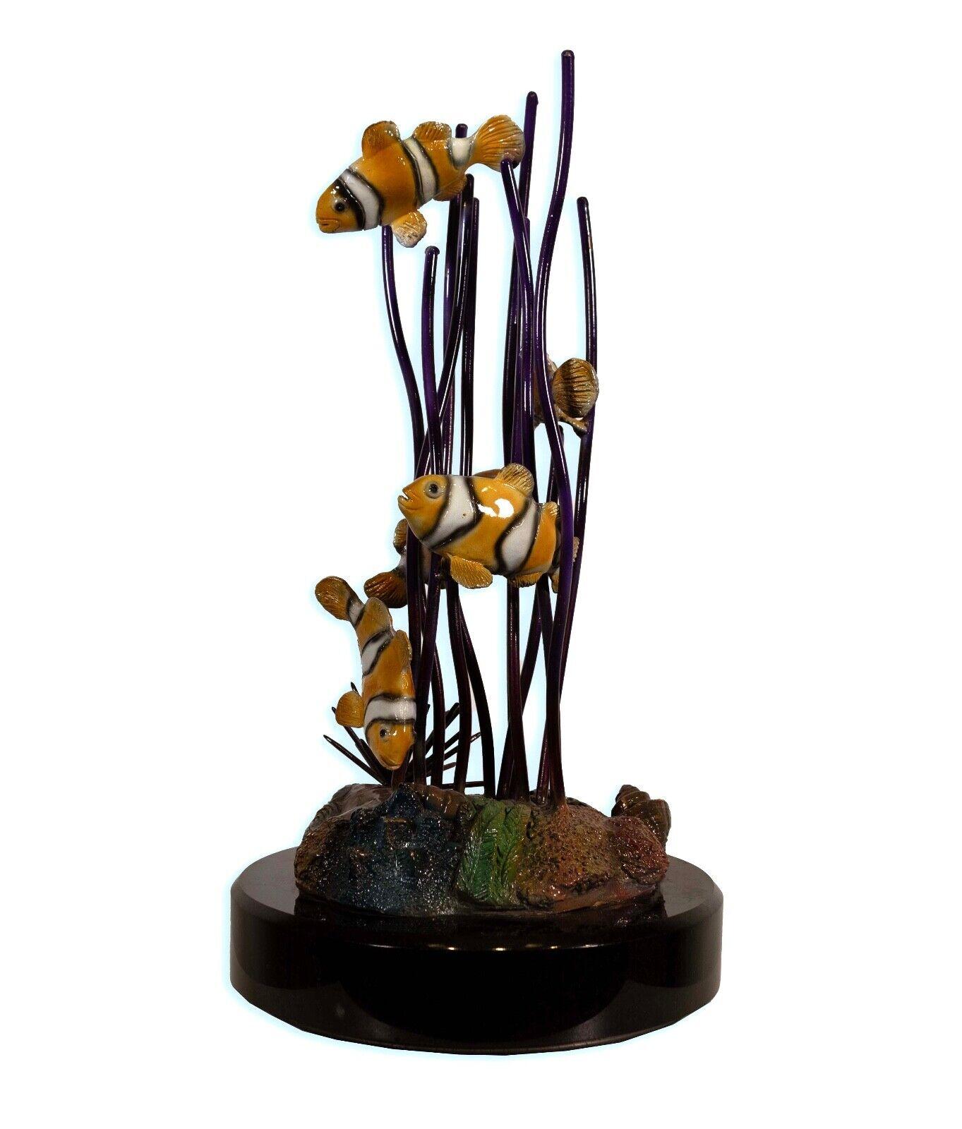 This sculpture by J. Townsend, numbered 7/399, presents a playful scene of clownfish among coral, crafted from a combination of bronze and ceramic. The fish are depicted with a high level of detail, their stripes and contours meticulously rendered,