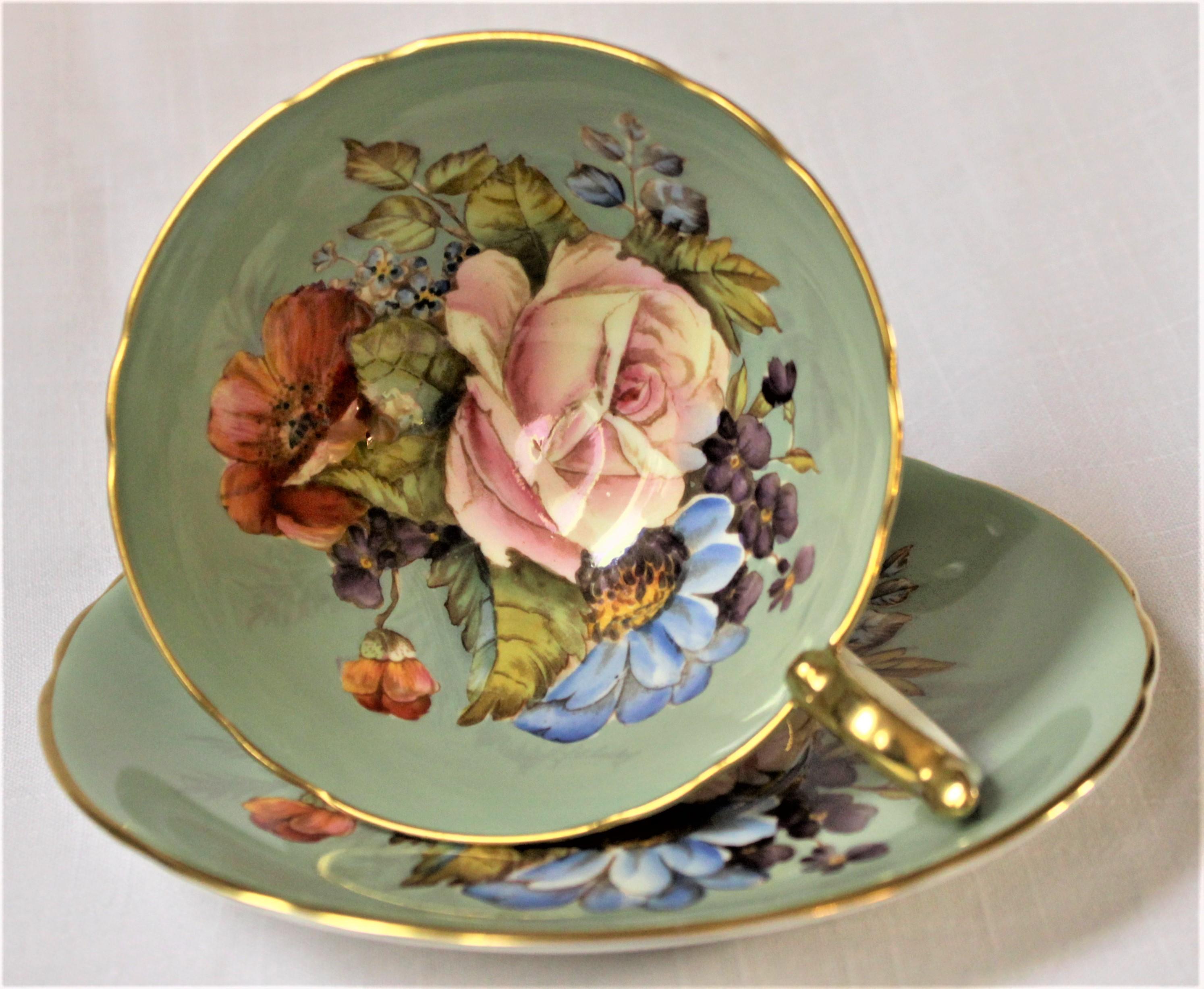 This very intricately hand painted tea cup and saucer set is made by the John Aynsley factory of England and are both are artist-signed by J.A. Bailey. This bowl of this cup is done with a floral bouquet with a large central pink cabbage rose. The