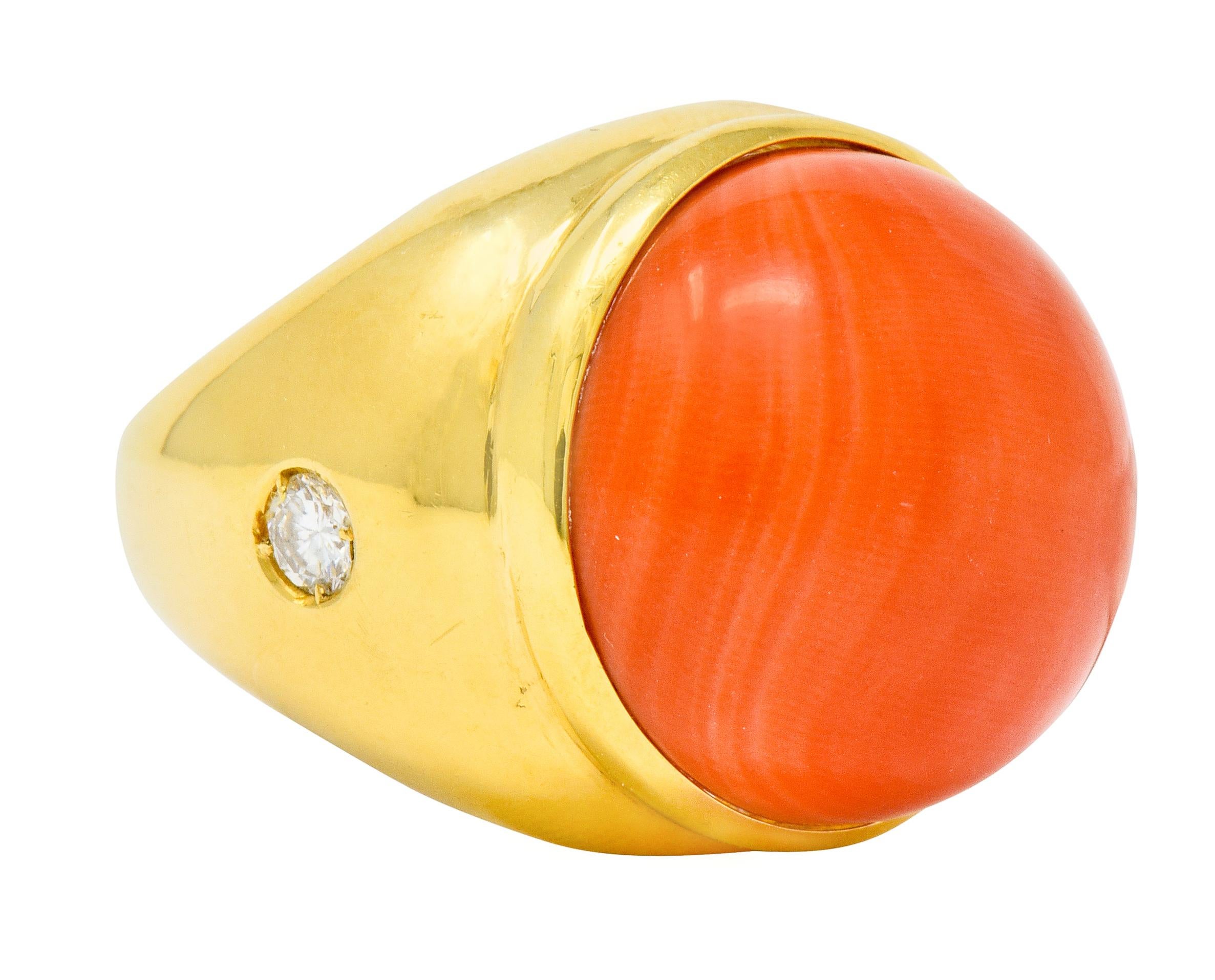 Centering a substantial 20.1 mm round coral cabochon, bezel set in a polished gold surround

Opaque and a robust orangey-red color with moderately swirled color distribution

Shoulders accented by flush set round brilliant cut diamonds weighing in