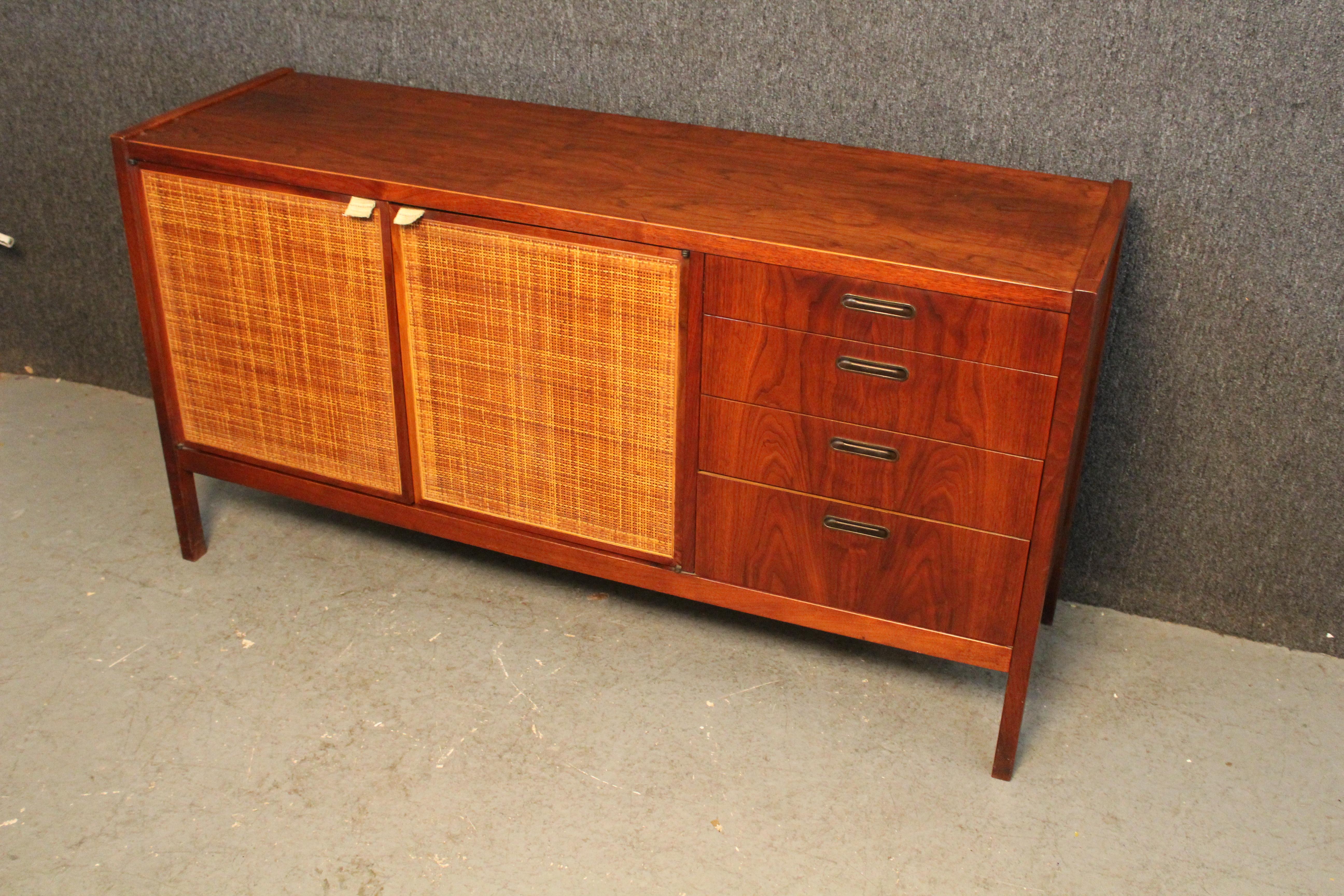 Fantastic petite sideboard from American Mid-Century Modern design legend, Jack Cartwright. Made for his iconic collection for Founders Furniture, it features beautiful woven cane panels paired against a rich walnut woodgrain. Four pull-out side