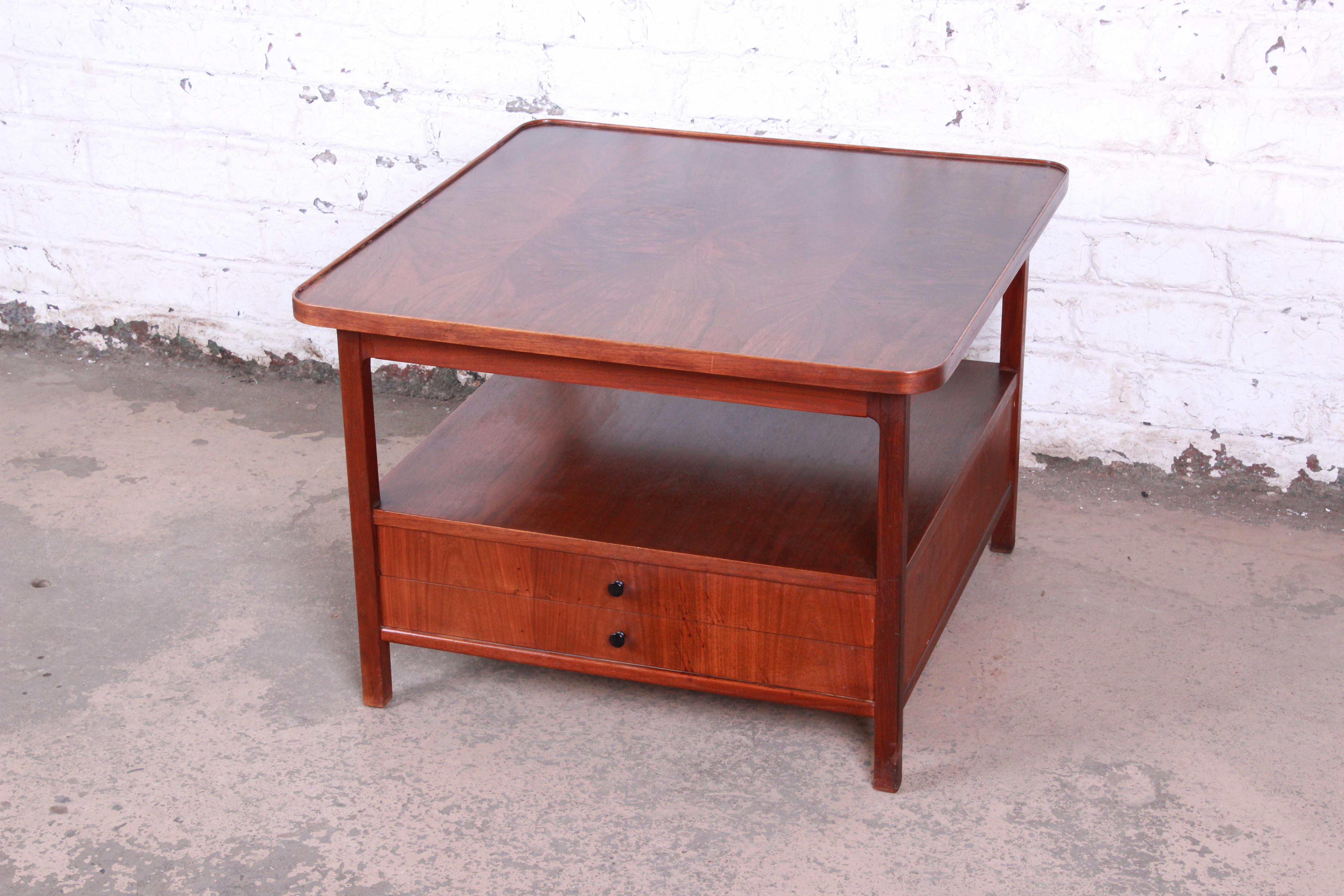 A gorgeous Mid-Century Modern rosewood two-tier cocktail table or occasional table by Jack Cartwright for Founders. The table features stunning wood grain with sleek mid-century design. It has two dovetailed drawers for storage. The table is in very