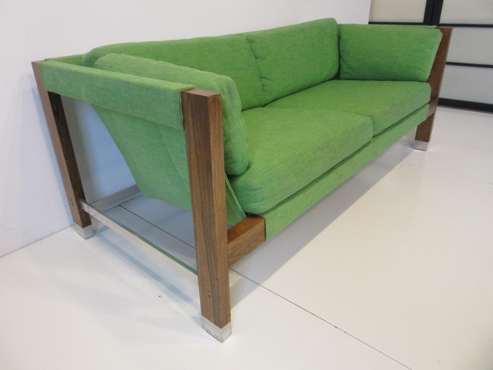 A upholstered sling styled sofa in apple green woven contract fabric with rosewood legs and aluminum tipped feet and stretchers. A well crafted piece from the 1970s designed by Jack Cartwright and retaining the label for the Founders Furniture