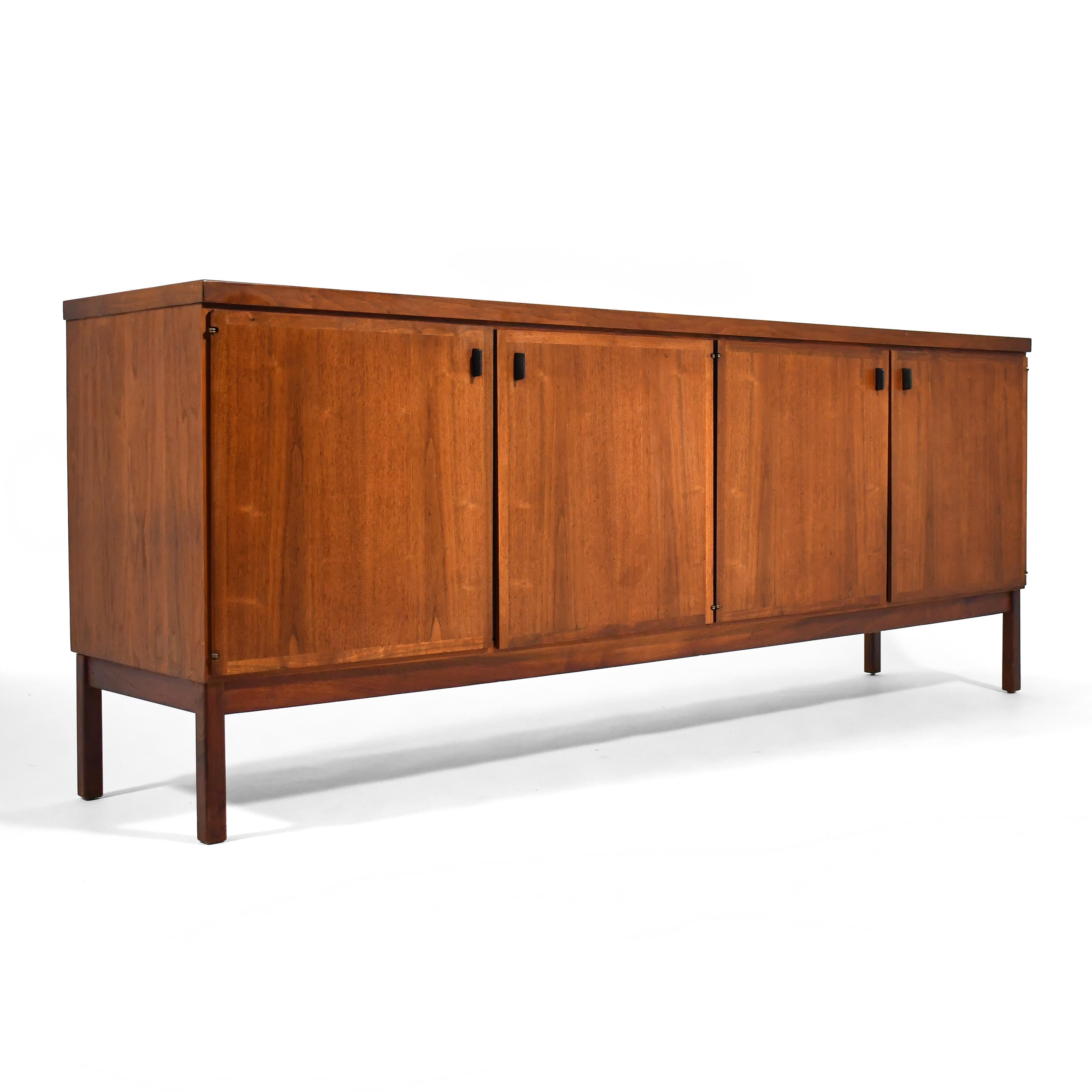 This handsome Jack Cartwright walnut credenza features two cabinets behind two doors each, one with a single adjustable shelf, the other with a silverware drawer and a linen drawer. Nicely detailed with a reveal between the top and the case, and