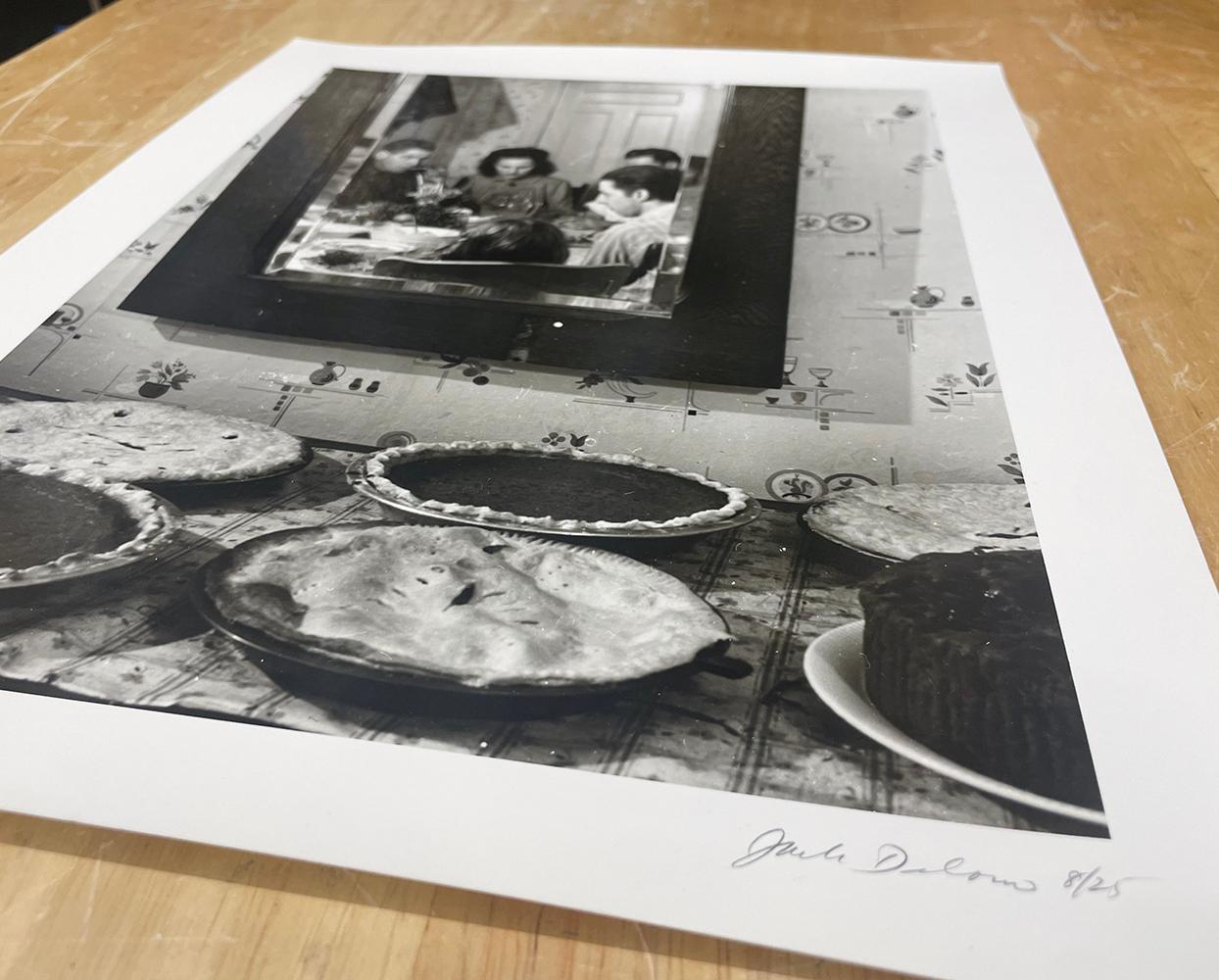 Thanksgiving Day, Ledyard, Connecticut von Jack Delano ist eine Schwarz-Weiß-Fotografie einer Familie, die ihre Thanksgiving-Mahlzeit einnimmt, gesehen durch die Reflexion eines Spiegels, mit Kuchen auf einem Tisch darunter.

Gelatinesilberdruck
12