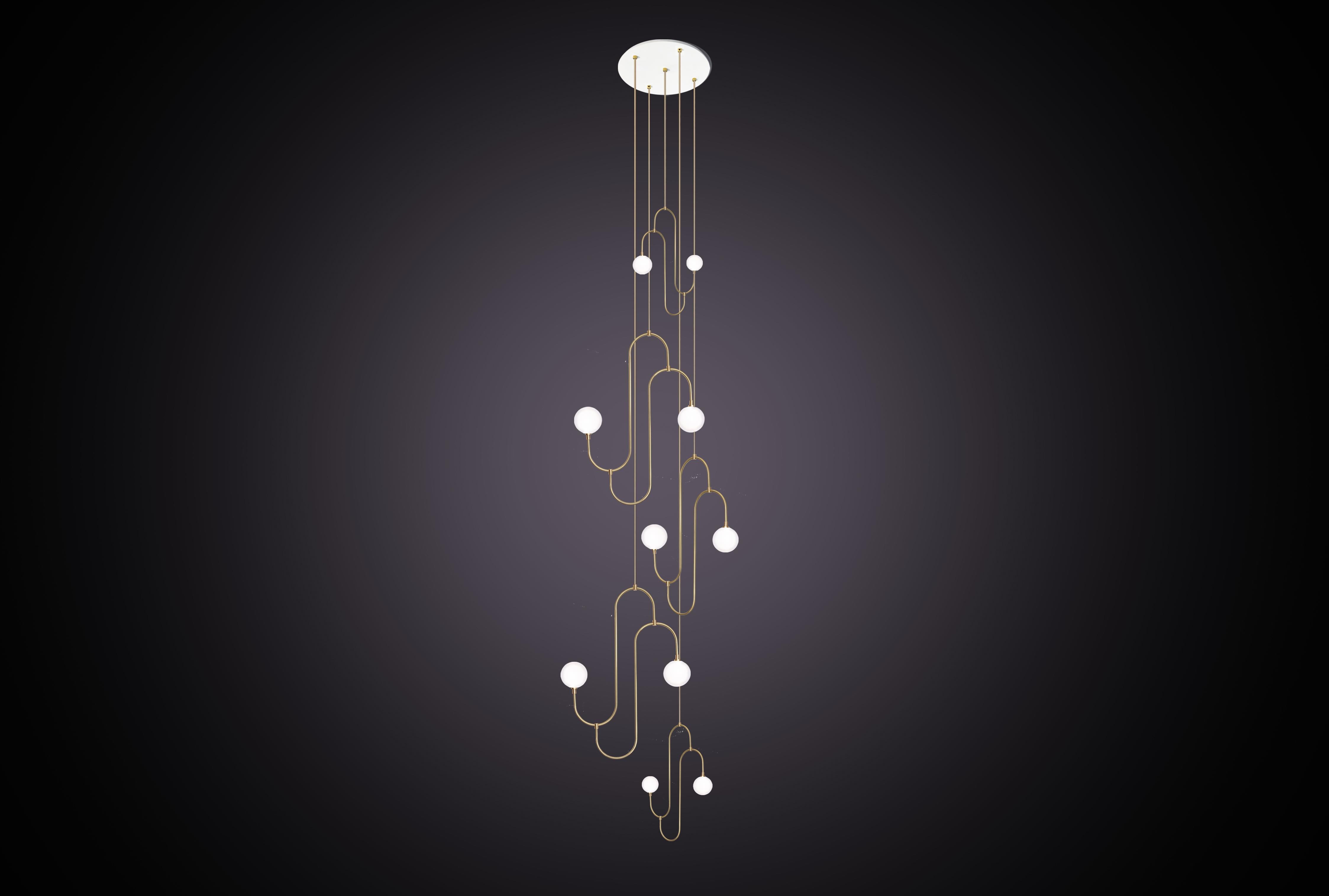 Inspiré par les motifs répétés et la forme sculpturale des bijoux des années 1930. La suspension incorpore des bras en laiton courbés à la main qui soutiennent le verre en cristal blanc perle, créant ainsi un élément d'éclairage décoratif et