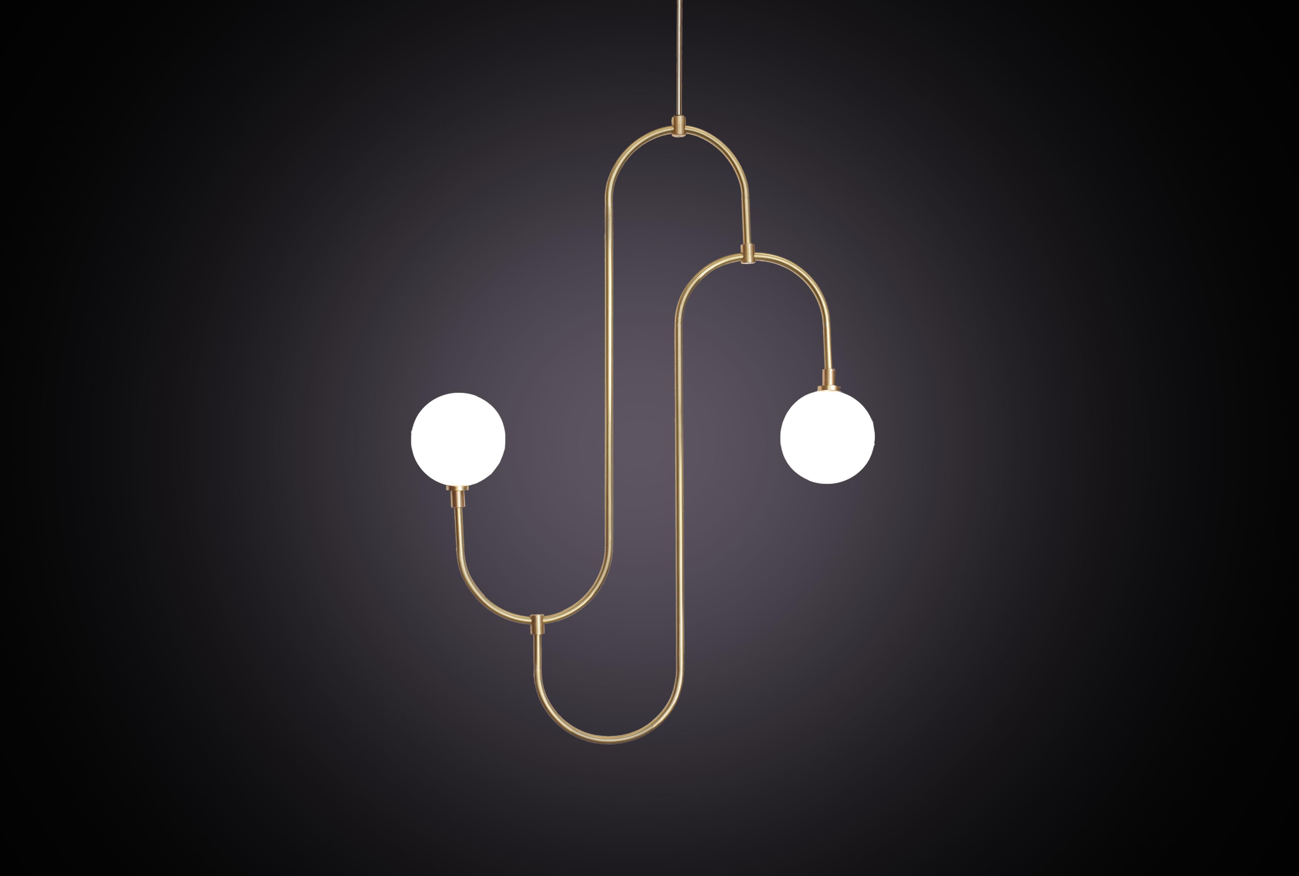 Si ispira ai motivi ripetuti e alla forma scultorea dei gioielli degli anni Trenta. Il pendente incorpora bracci in ottone piegati a mano che sostengono il vetro di cristallo bianco perlato, creando un elemento di illuminazione decorativo e