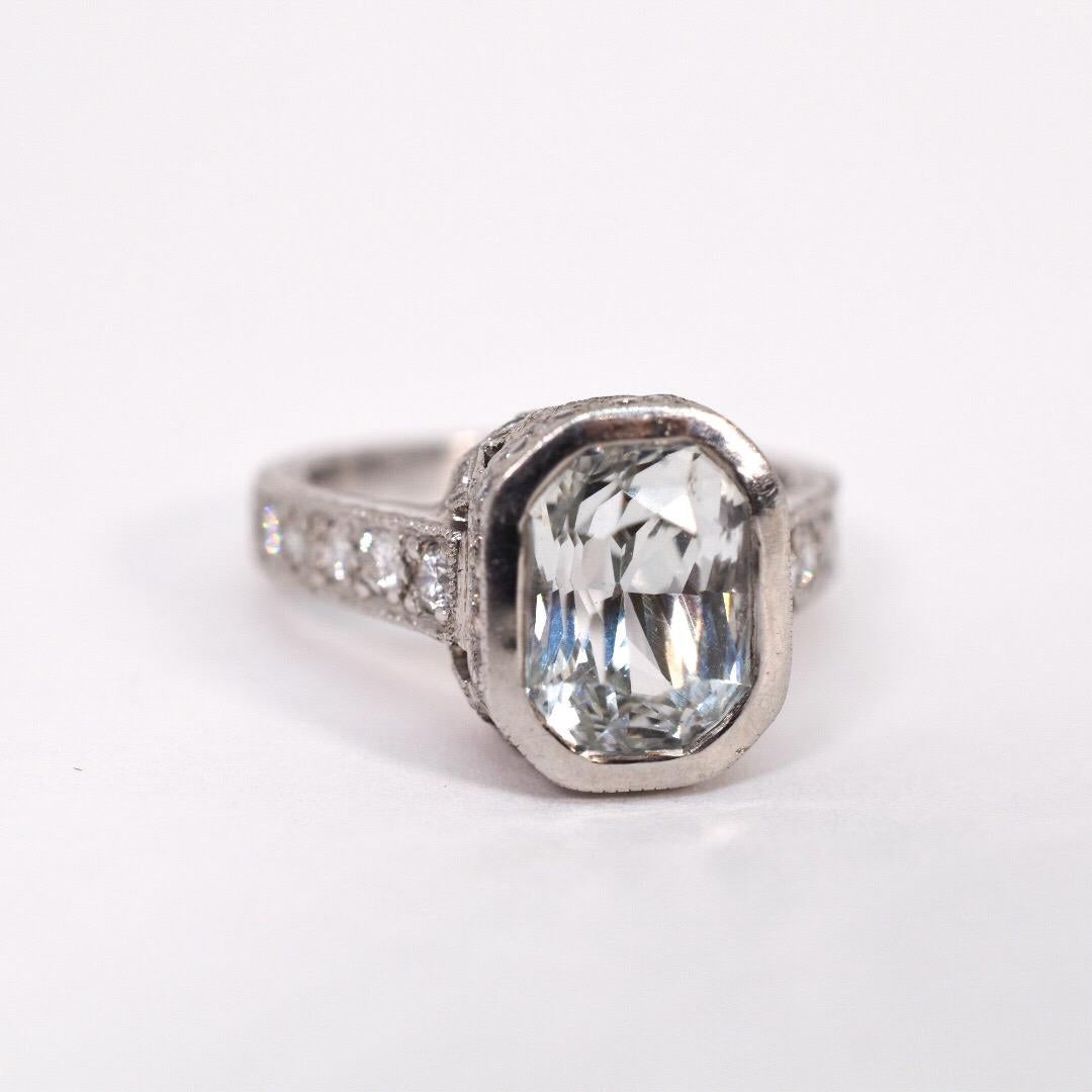 Platinum engagement ring designed by Jack Kelege set with a natural radiant cut white sapphire and round brilliant cut diamonds. The center white sapphire is bezel set with accenting diamonds around the head and halfway around the shank. Hand