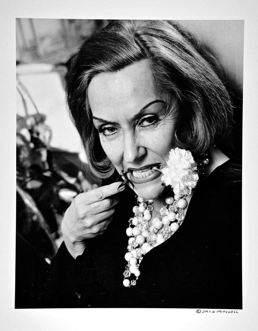 Fotografía vintage de gelatina de plata de 11 x 14 pulgadas de la superestrella de la gran pantalla Gloria Swanson posando dramáticamente con un clavel blanco, su flor característica, en su apartamento de Nueva York en 1965. Procede directamente de