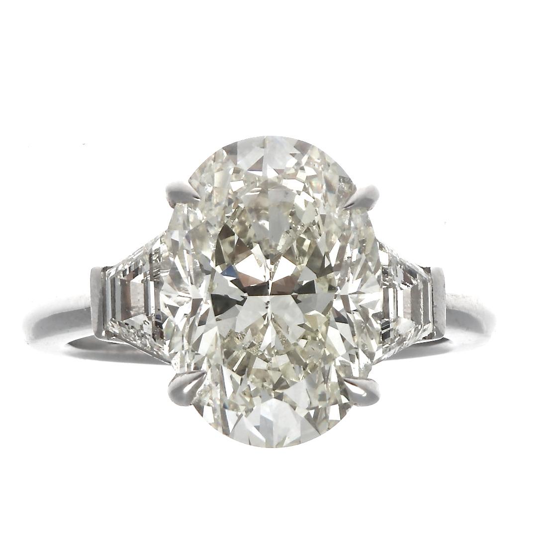 Synonymous with love the diamond engagement ring represents an everlasting bond between lovers. Featuring a 5.15 carat oval cut diamond that is approximately N,O   color, SI1 clarity. Accented  by trapezoid diamonds. Ring size 7 and can easily be