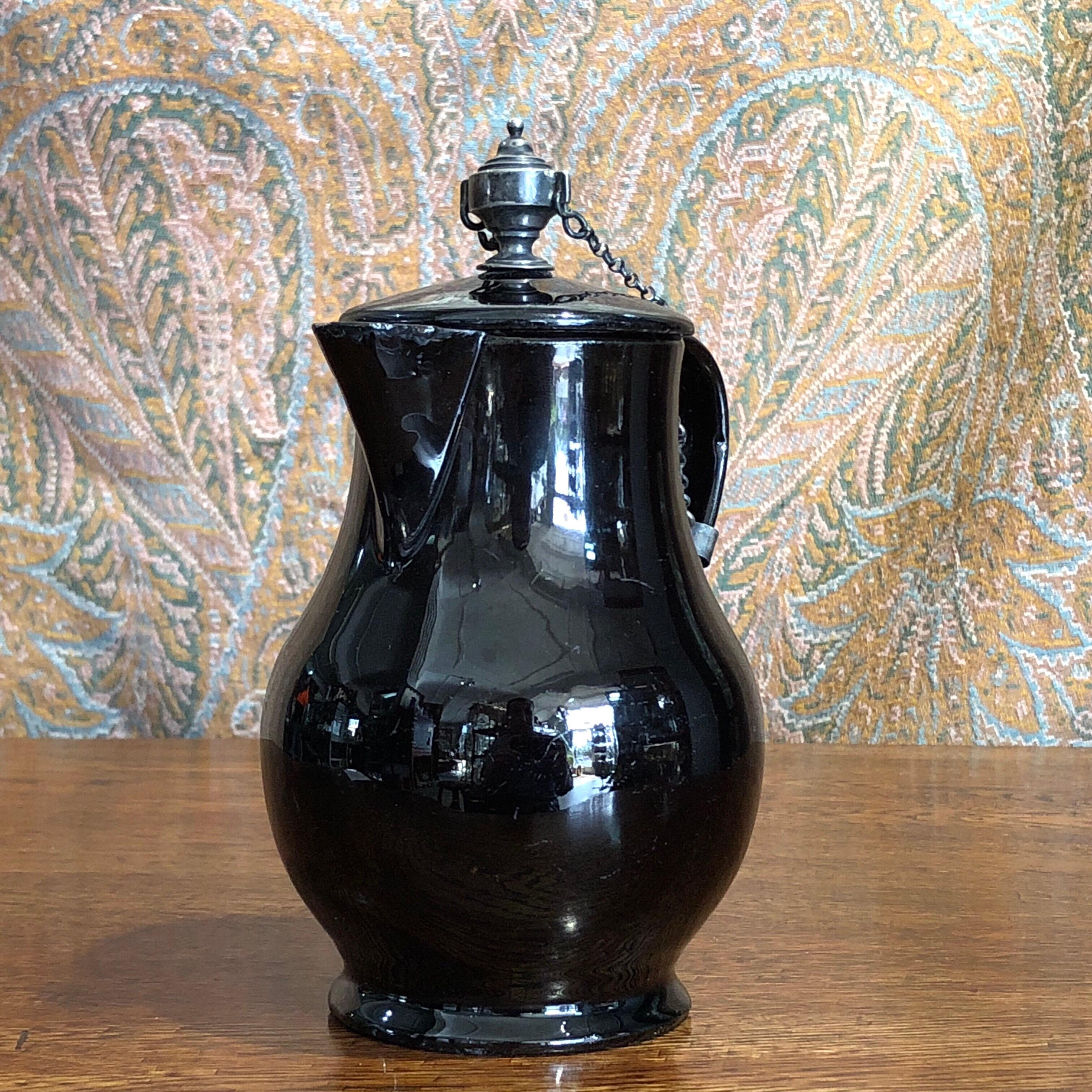 Jackfield type jug and cover, the baluster form with glossy black glaze, the handle terminal turned into an animal head, the lid with a sophisticated silver urn knop, probably an earlier replacement, with twin chains attaching to a collar at the