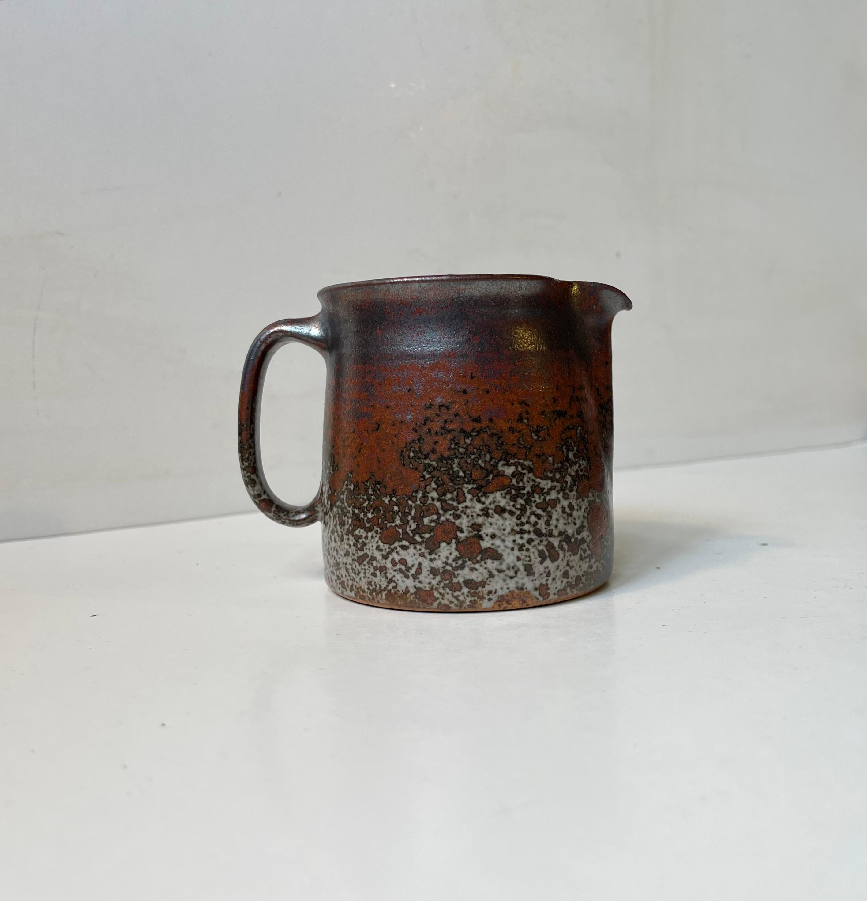Small exceptional stoneware jug heavily decorated with earthy crystalline glazes by Jacob Bang. The kid brother of Arne Bang. Made in Jakob E. Bangs studio during the early 1960s. Signed by the designer to the base. Measurements: H: 9 cm, D/W: