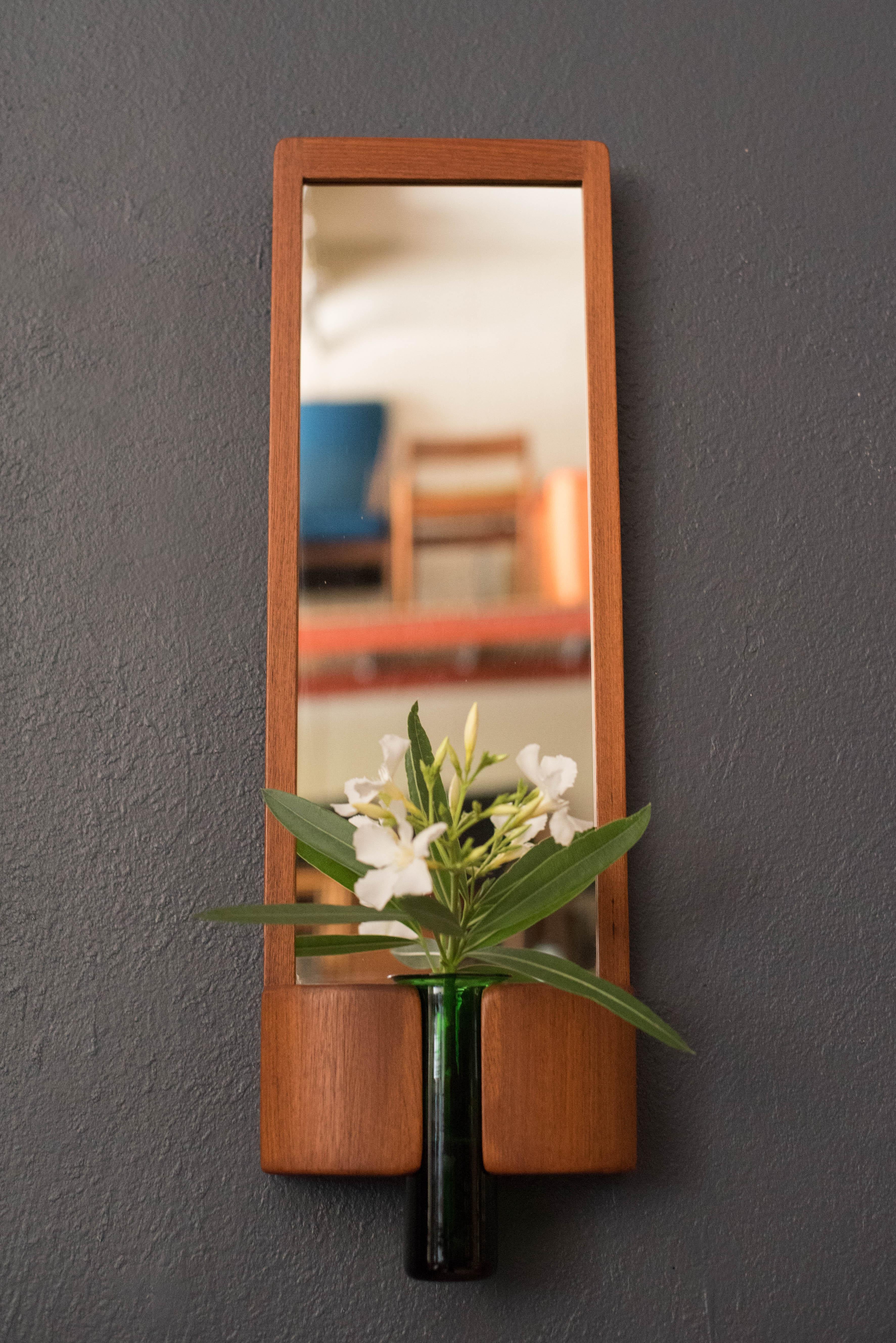 Mid-Century Modern hanging wall mirror designed by Jacob Hermann for Randers Møbelfabrik, circa 1960s, Denmark. Features a sculptural teak frame with detailed joinery and includes the original emerald green glass vase by artist Per Lütken of