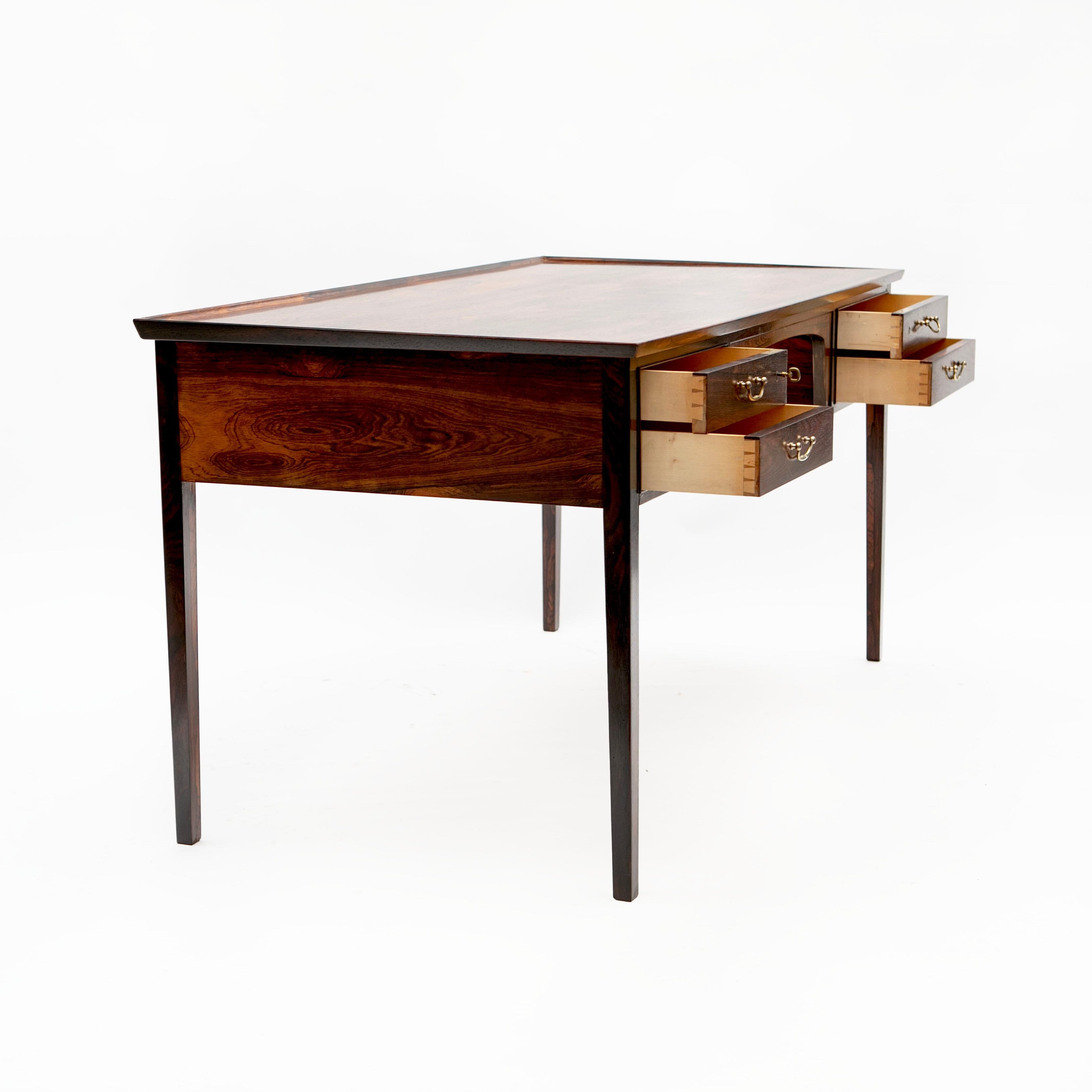 Freestanding Rio rosewood writing desk with beautiful grain designed by Jacob Kjær, Denmark 1950-1960.
Front with 2x2 drawers with brass pulls. Top with raised edge.
The desk shows remarkable high-quality craftsmanship and is equipped with many