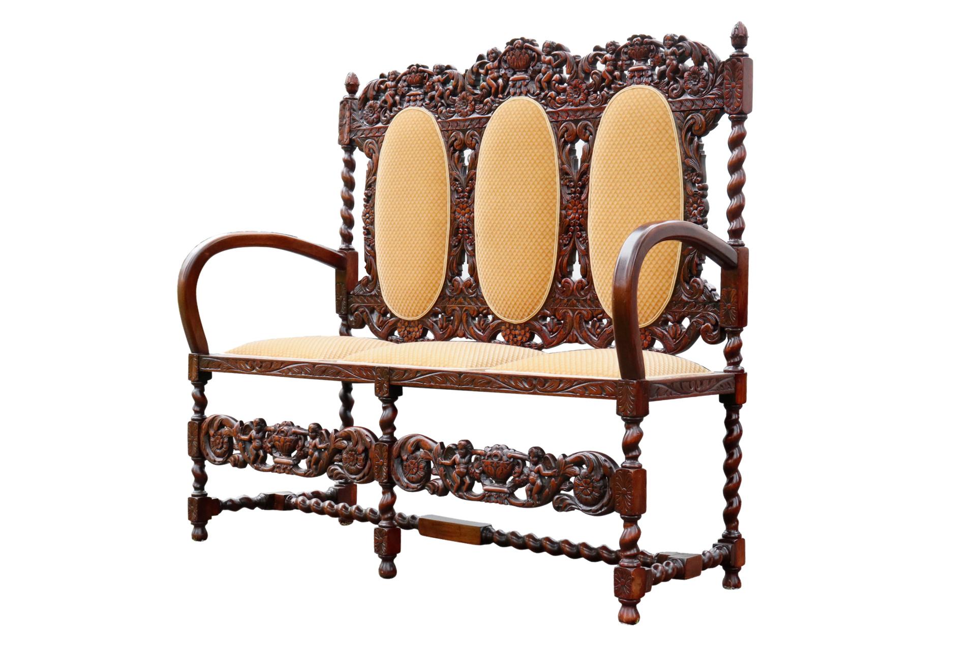 A richly carved Jacobean three seat settee made of oak. Square seat cushions and oval back cushions are upholstered in a traditional diamond cut yellow velvet. The seat back is carved with scrolled acanthus leaves and berry trimmed rosettes,