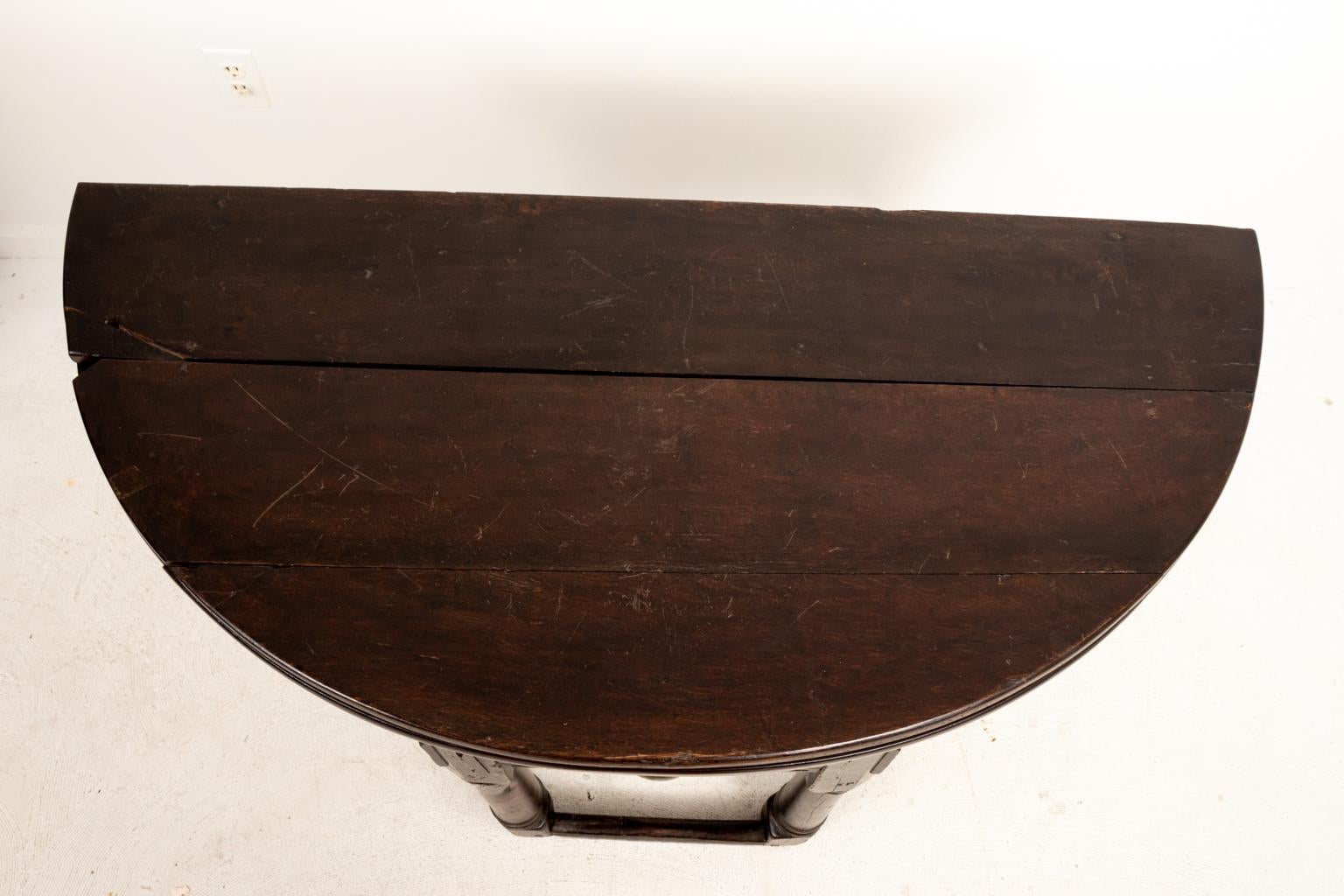Crédence ou table pliante de style jacobéen à un tiroir et plateau en demilune incurvé, vers le XVIIe siècle. La pièce présente également une jupe fortement sculptée, des pieds tournés en anneau et une traverse inférieure. Fabriqué en Angleterre.