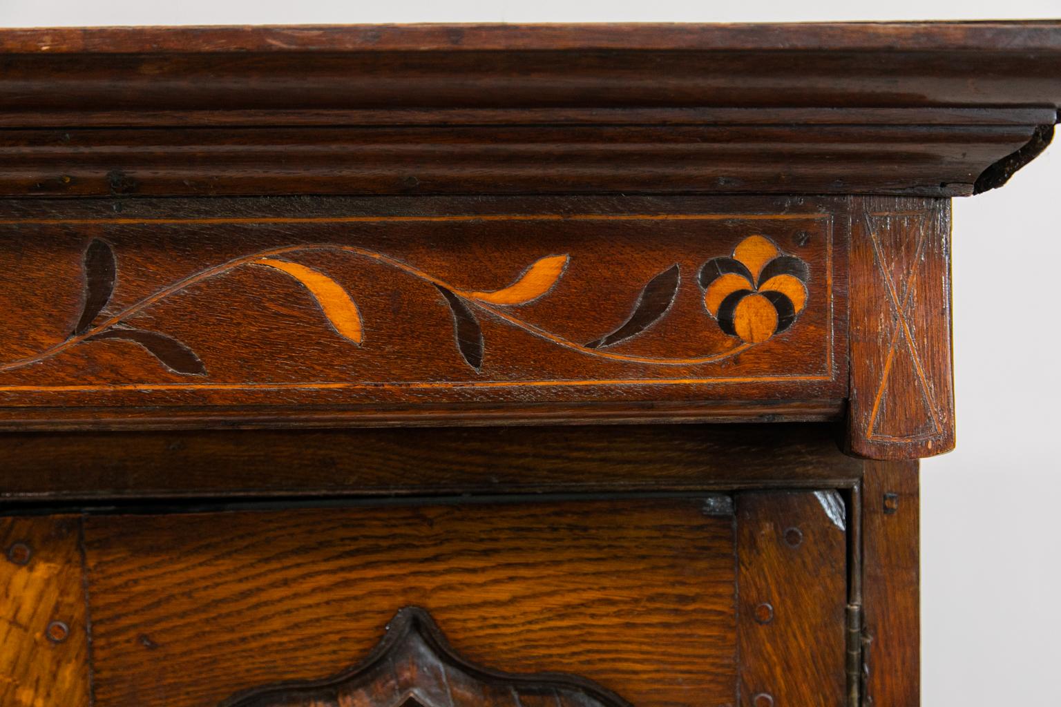 Jacobean inlaid barley twist court cupboard is inlaid with satinwood and ebony arabesques. There is exposed triple peg construction with a carved molded stretcher terminating in bun feet.