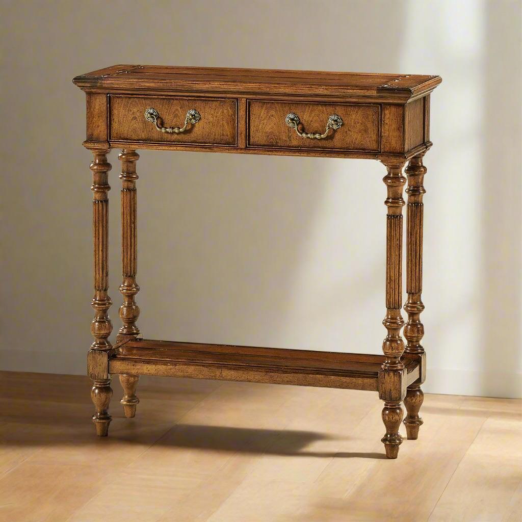 Designed in an antique walnut finish, this console features a planked top and shelf, lending a rustic charm to its classic silhouette. The two drawers, adorned with custom cast brass hardware, provide discreet storage while maintaining the table’s