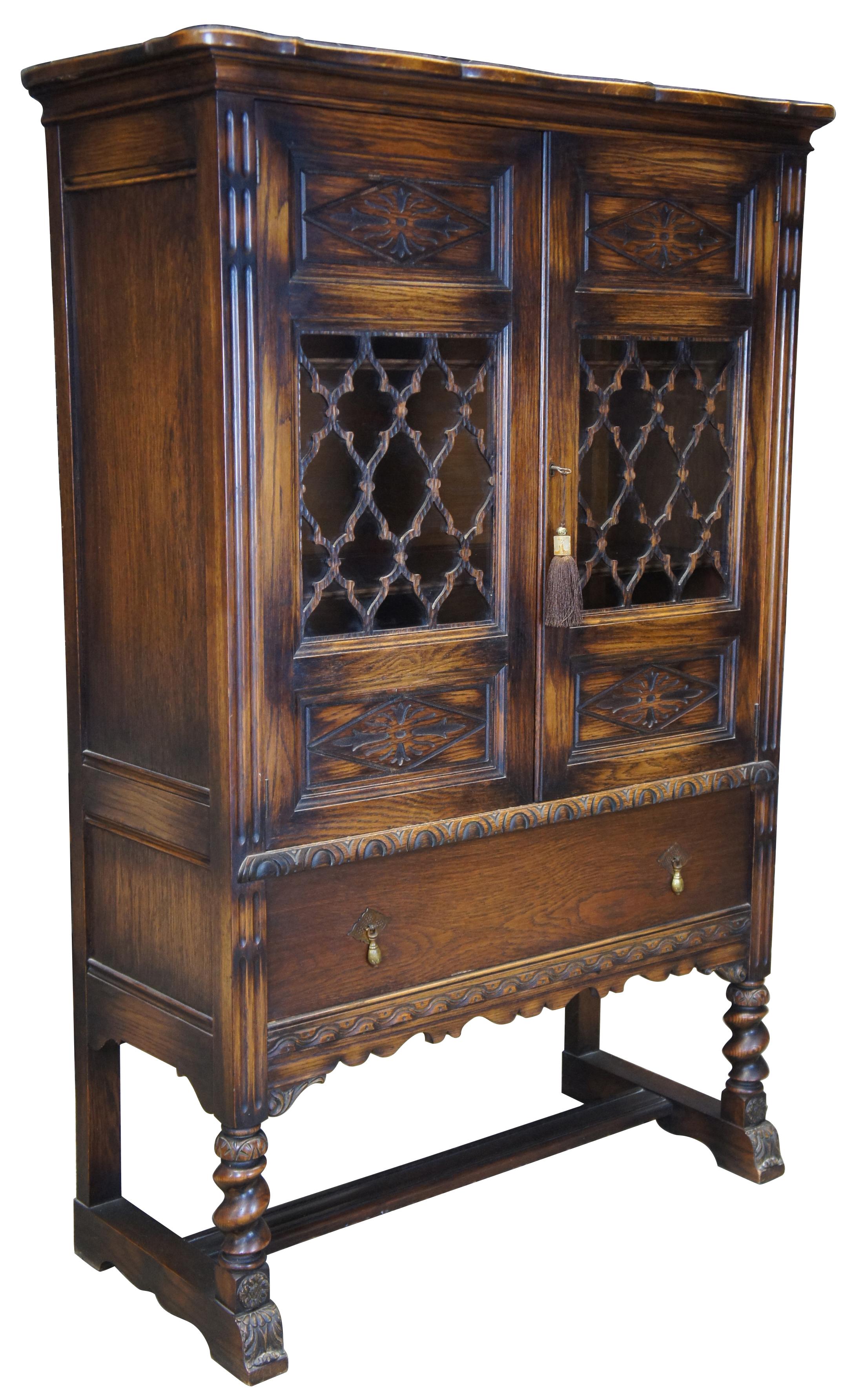 Early 20th century Jacobean or Spanish Revival china cabinet. Made from oak with two diamond paneled doors featuring lattice fretwork over glass doors. Doors open to three shelves with plate grooves. The cabinet features one large lower drawer for