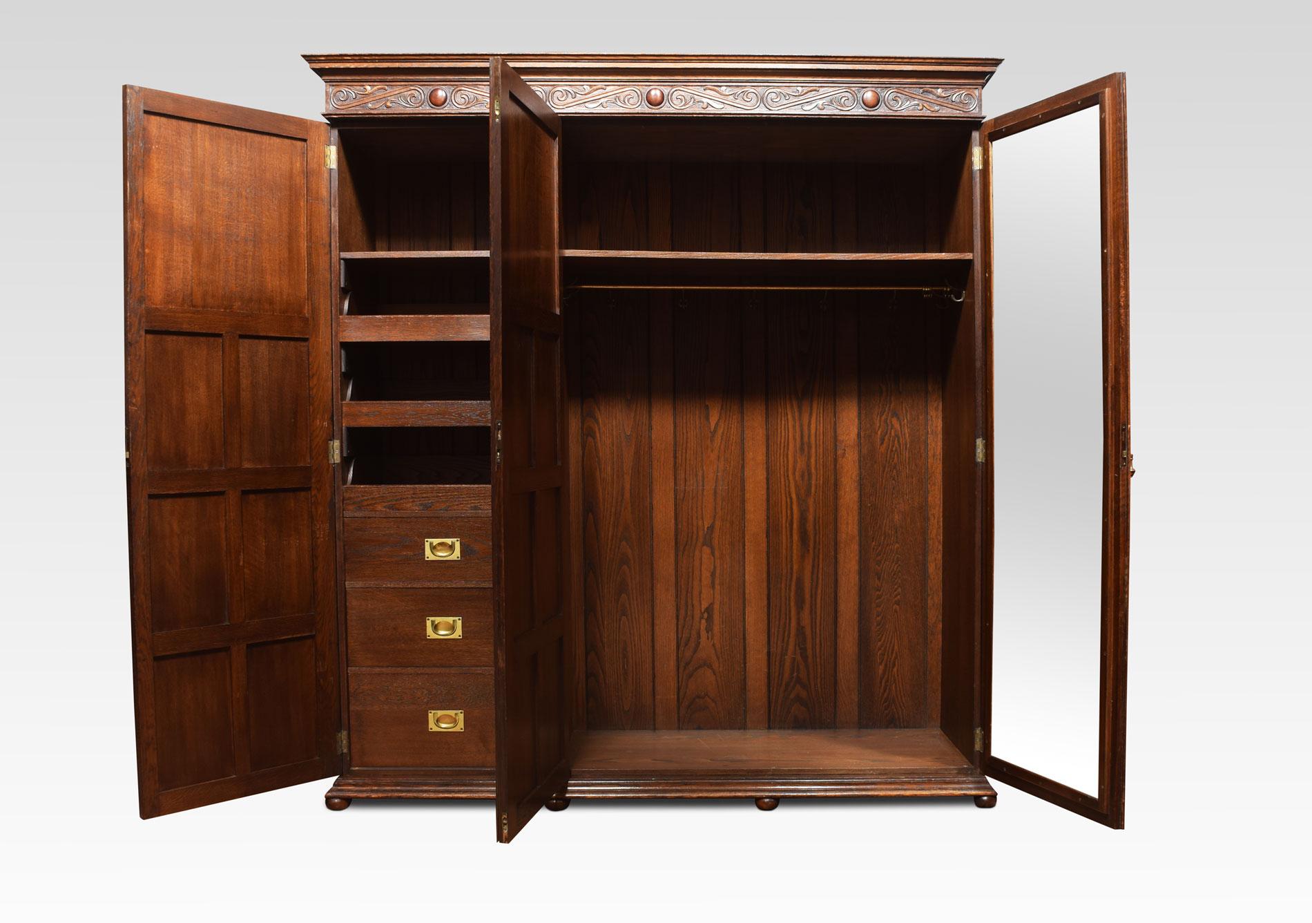 Large solid oak three-door compactum wardrobe. The moulded cornice with blind frett freeze above three geometric panelled doors opening to reveal an internal mirror, large hanging area to one side the other fitted with three drawers and three linen