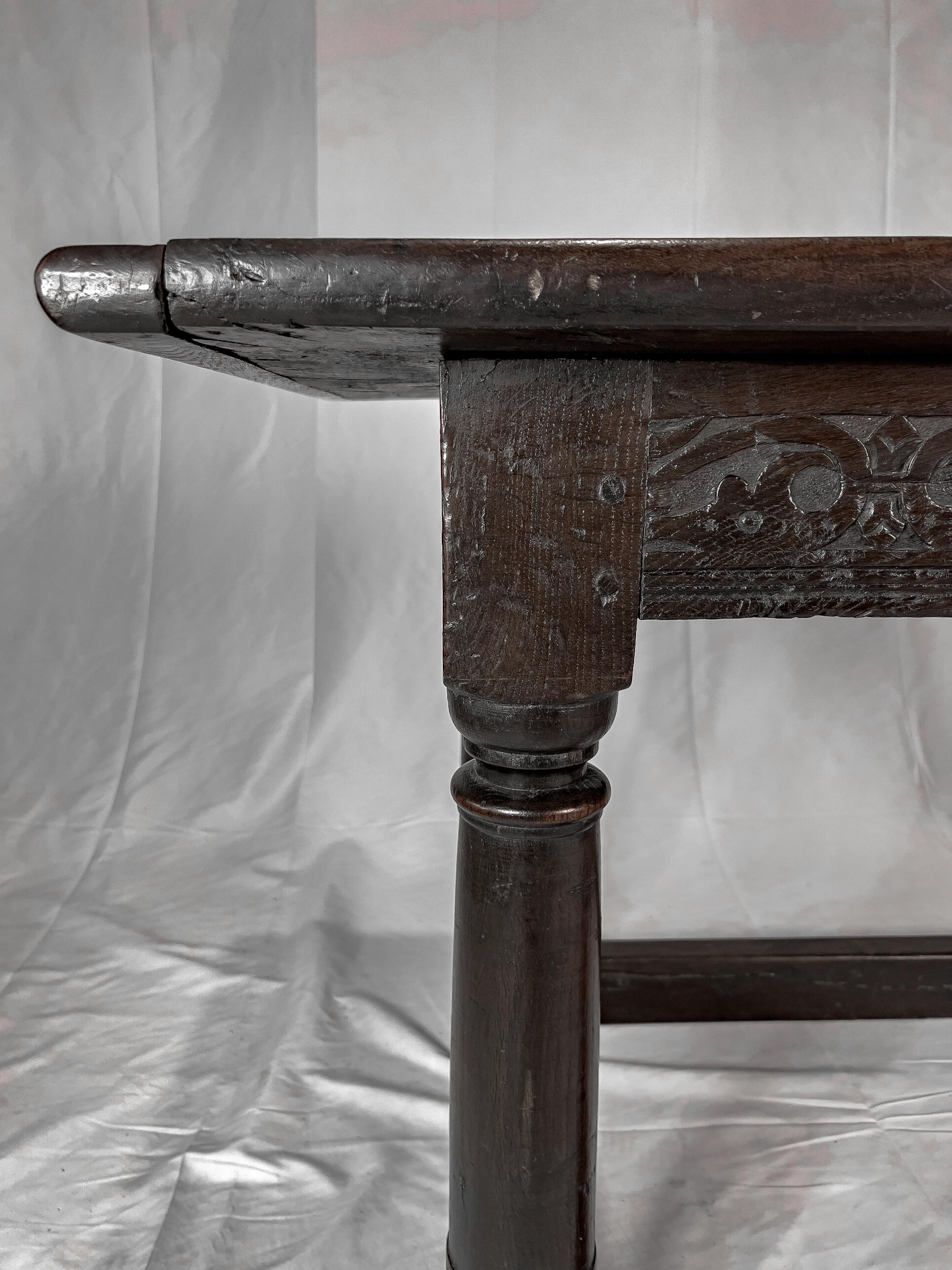 Circa 1810 English oak Jacobean style Table with a plank top, hand-carved detail along all 4 sides of the apron, and 4 heavy turned legs joined with a stretcher.