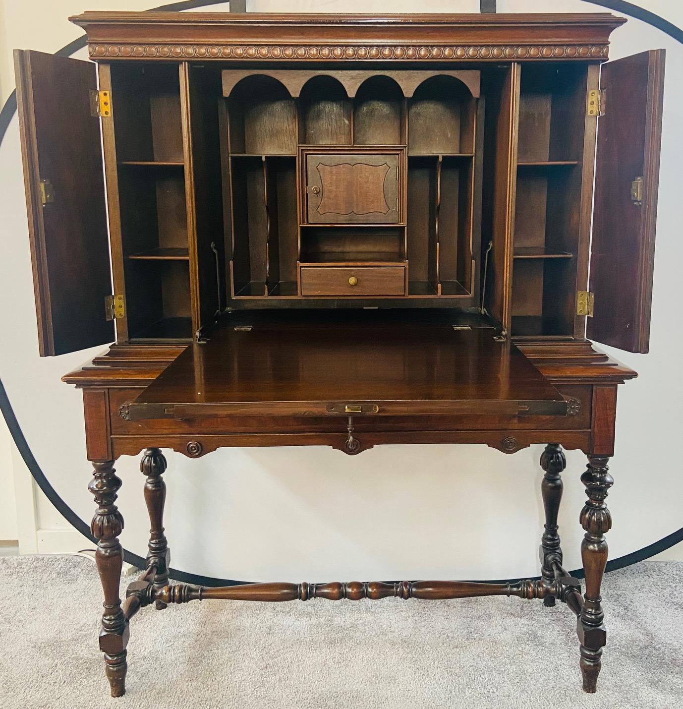 A 1970's Jacobean Spanish colonial style drop-lid slant front desk made of quality flame mahogany with upper double side door cabinets. Featuring a solid mahogany construction with a beautiful flame veneer, the desk offers multiple open compartments