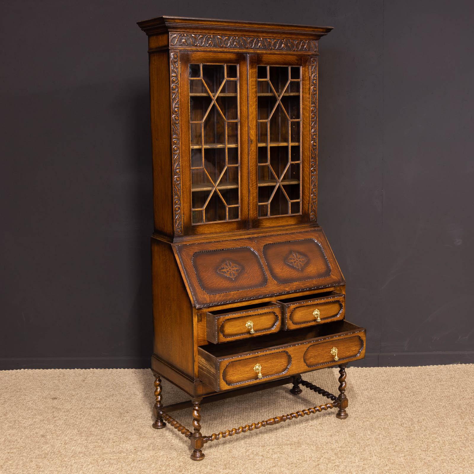 A quality oak bureau bookcase from the 1920s, the turned feet support the twist stretchers and legs above which are one long and two short drawers all with original polished brass knobs. The sloping fall has blind fretwork decoration and inside is a