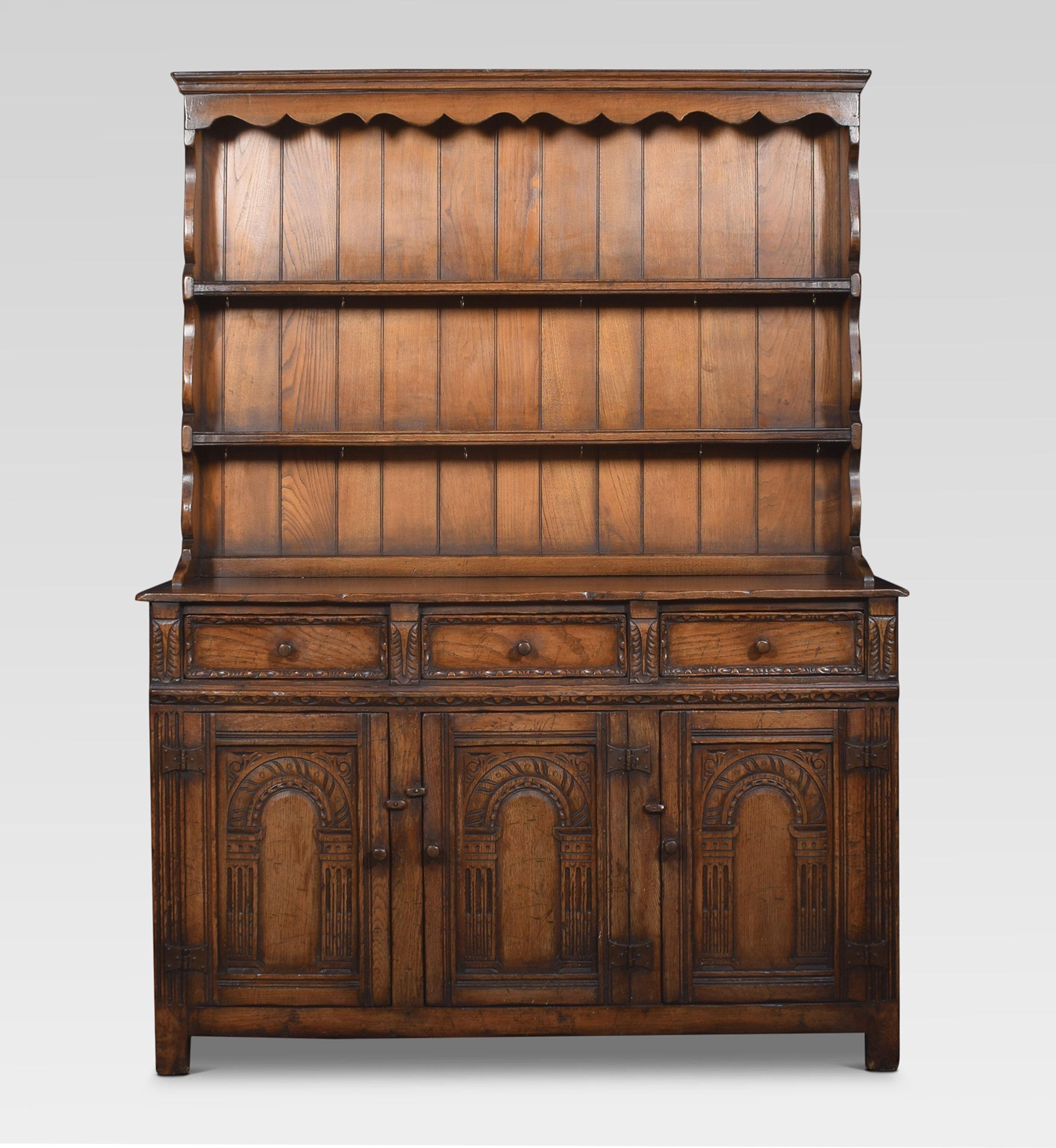 Jacobean style oak dresser, the top rail above plate rack with two shelves. The base having a large rectangular top above three frieze drawers and three panelled cupboard doors below, opening to reveal a large storage area. All raised up on bracket