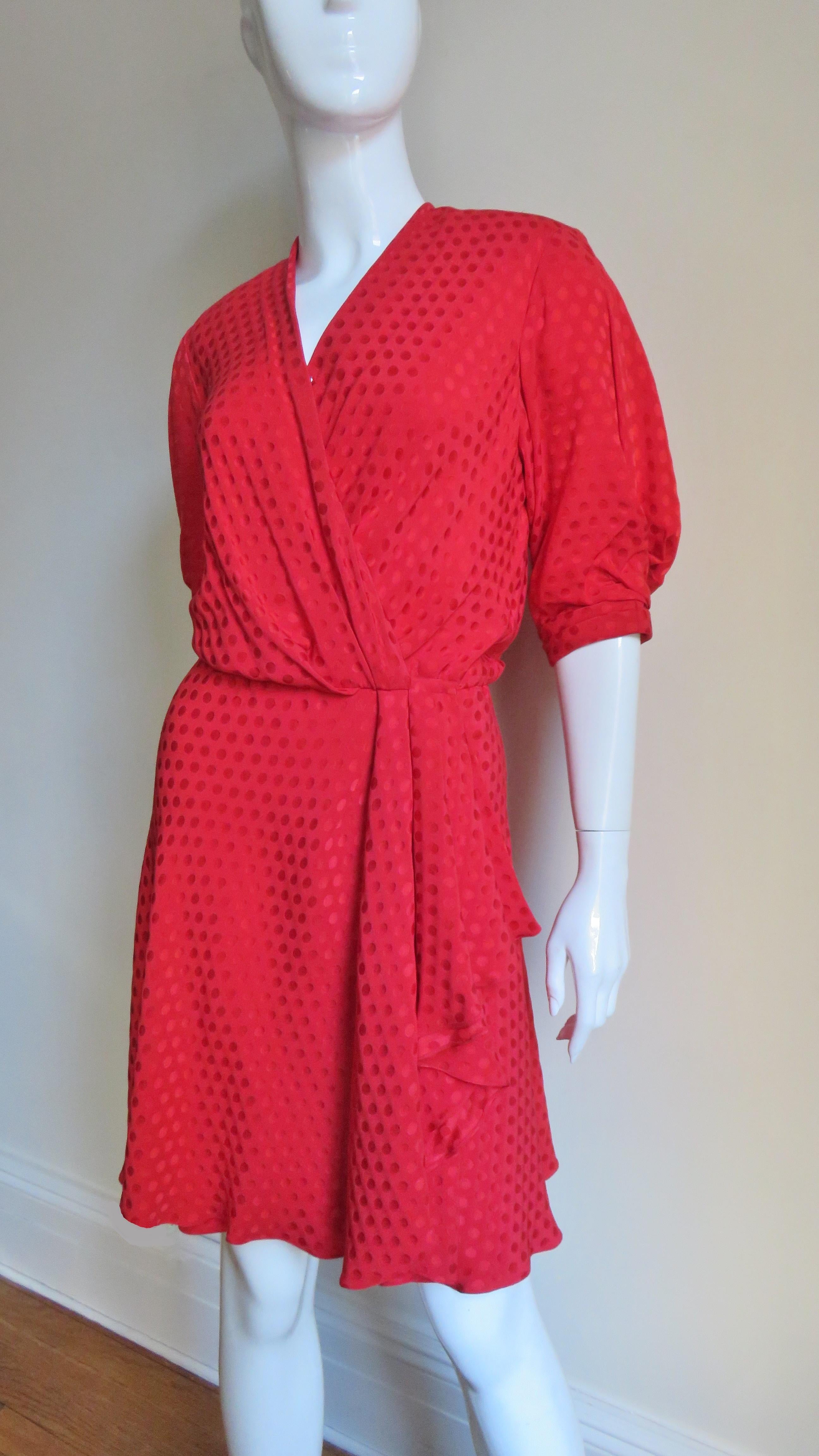 A beautiful red dot silk damask dress from French designer Jacqueline de Ribes.  It wraps across the front closing with a hook at the waist, matching silk covered snaps and a small zipper below it.  It has a V neck, draped blouson bodice and full,