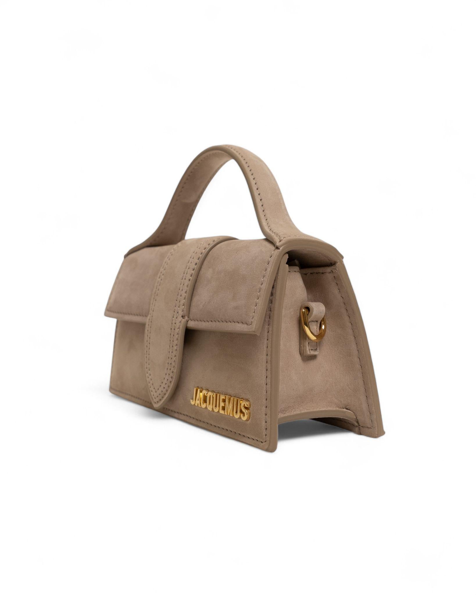 Jacquemus signature bag, model Le Bambino in size Mini, made of beige suede fabric with gold hardware. Features a front flap with magnetic closure, internally lined with beige canvas, roomy for essentials. Equipped with a handle and a removable,