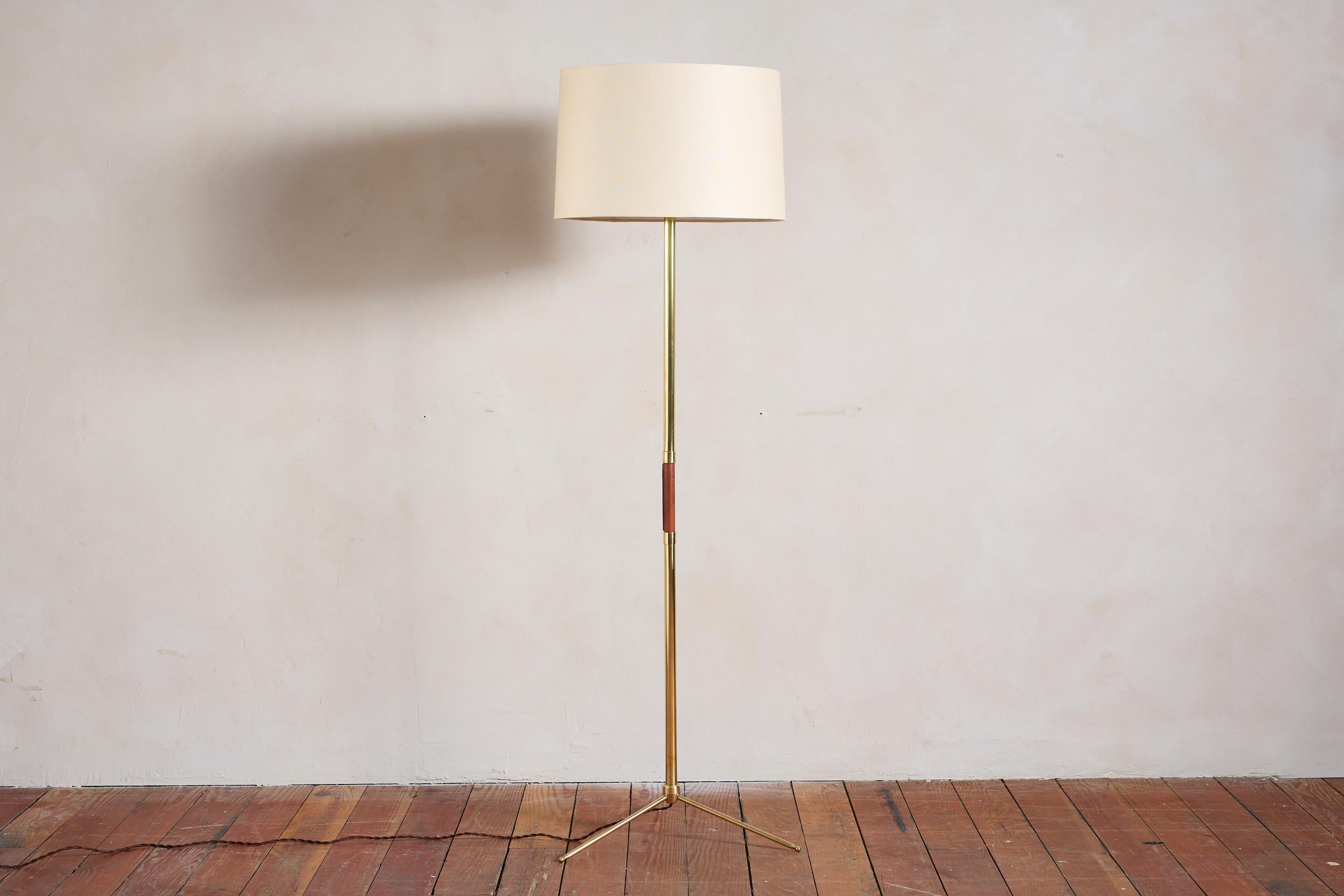 Beau lampadaire français de Jacques Adnet.

Mât en laiton avec détail central en cuir brun selle cousu à la main, coutures contrastées, base de trépied en laiton et nouvel abat-jour en lin. 

Nouvellement recâblé. 